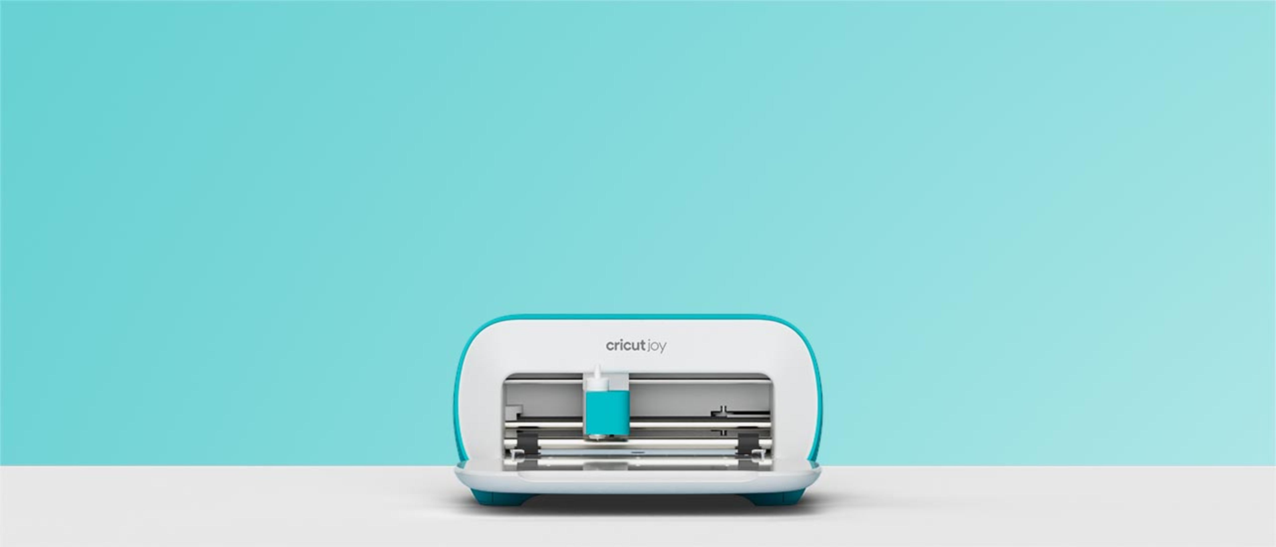 Eine türkisfarbene Cricut Joy Maschine auf einer weißen Oberfläche, mit türkisfarbenem Hintergrund.