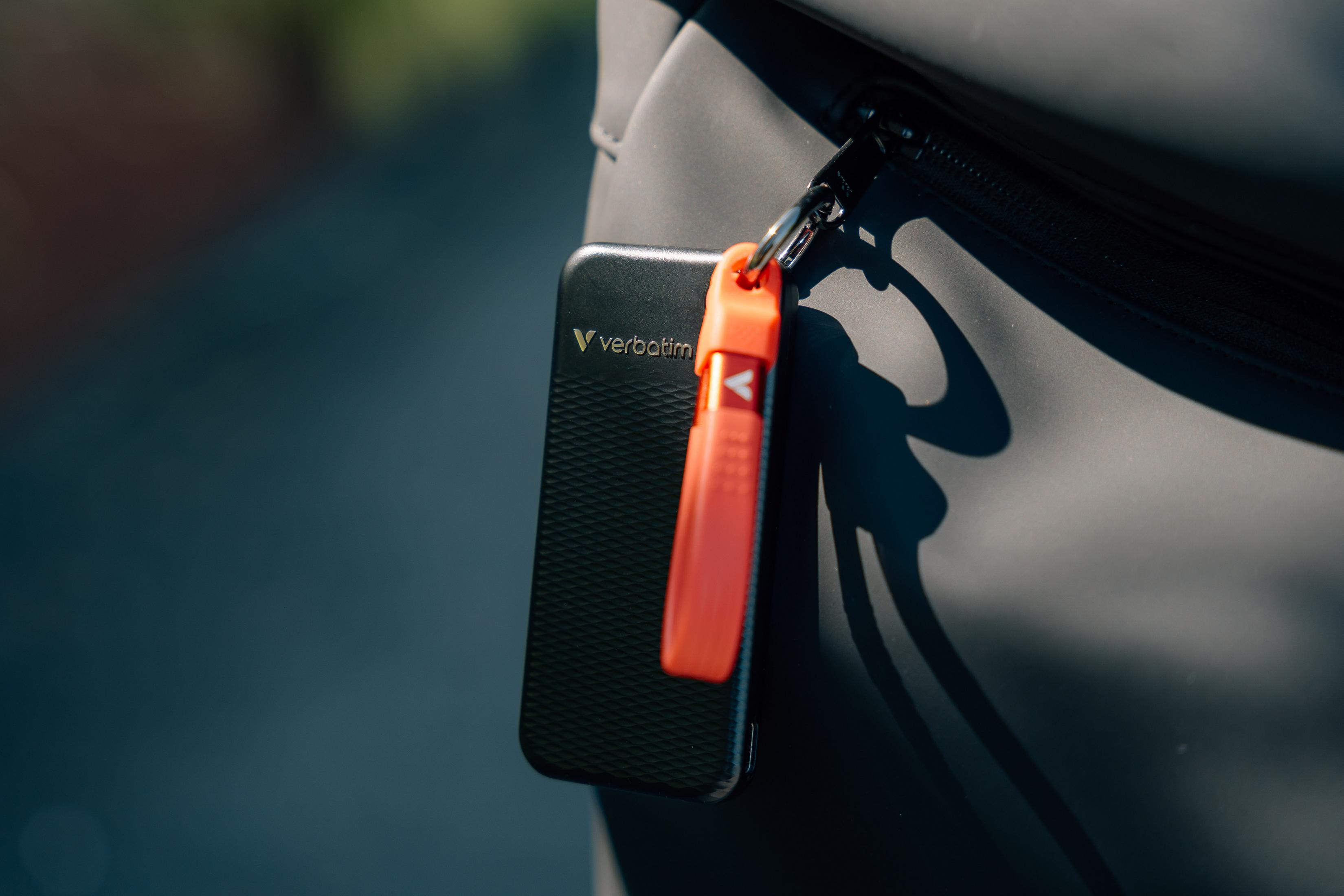 Czarny zewnętrzny dysk twardy Verbatim z dołączonym czerwonym paskiem, na ciemnej powierzchni. Widoczny zamek błyskawiczny.