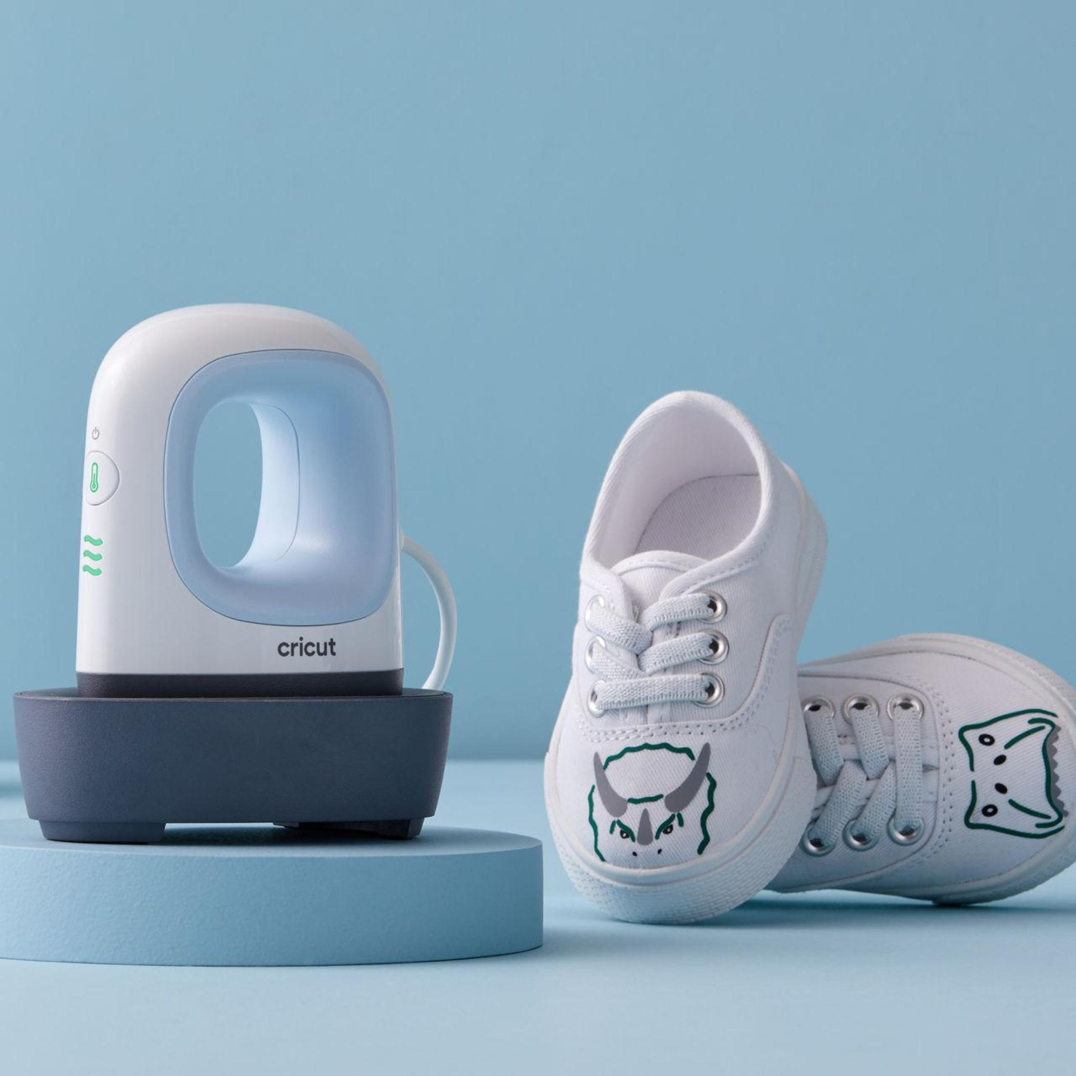 Una prensa de calor Cricut con zapatos blancos con arte de dinosaurios.