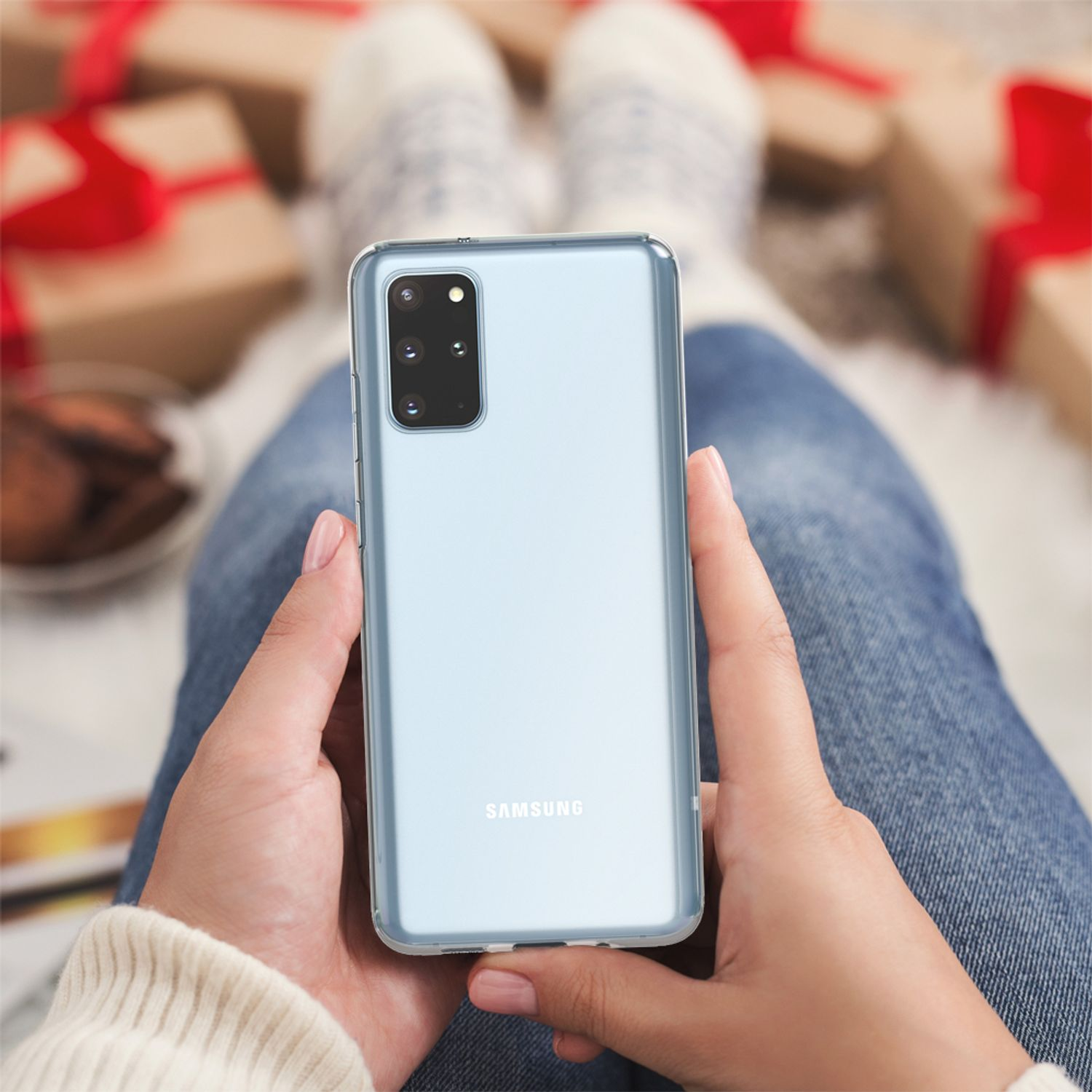 Mani che tengono un telefono blu, jeans e calzini, con regali sullo sfondo.