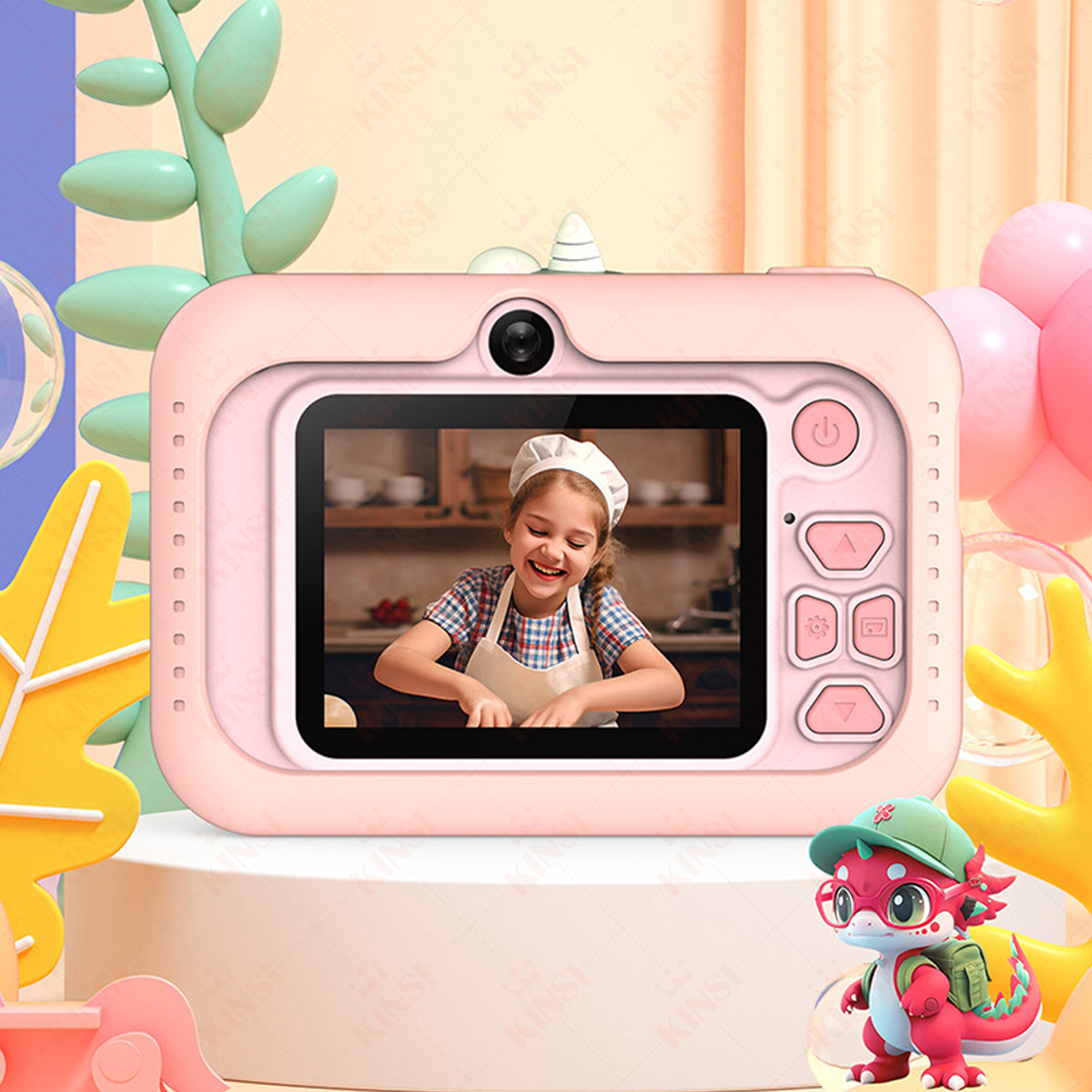 Różowy aparat zabawka z ekranem pokazującym dziewczynkę. Zielona zabawka smoka jest na dole po prawej.