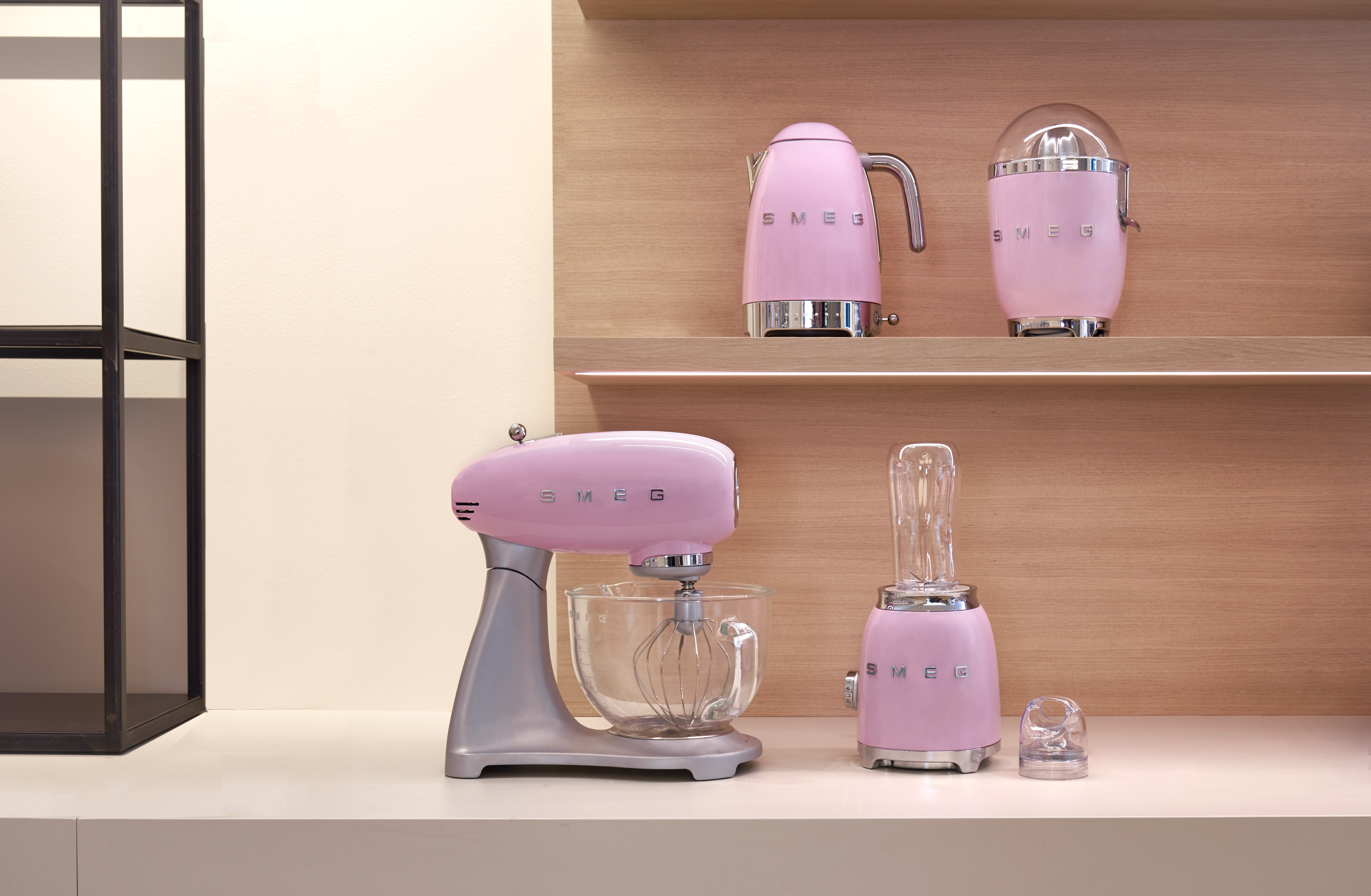 Pembe SMEG mutfak aletleri: bir mikser, bir blender, bir su ısıtıcısı ve bir narenciye sıkacağı bir rafta.