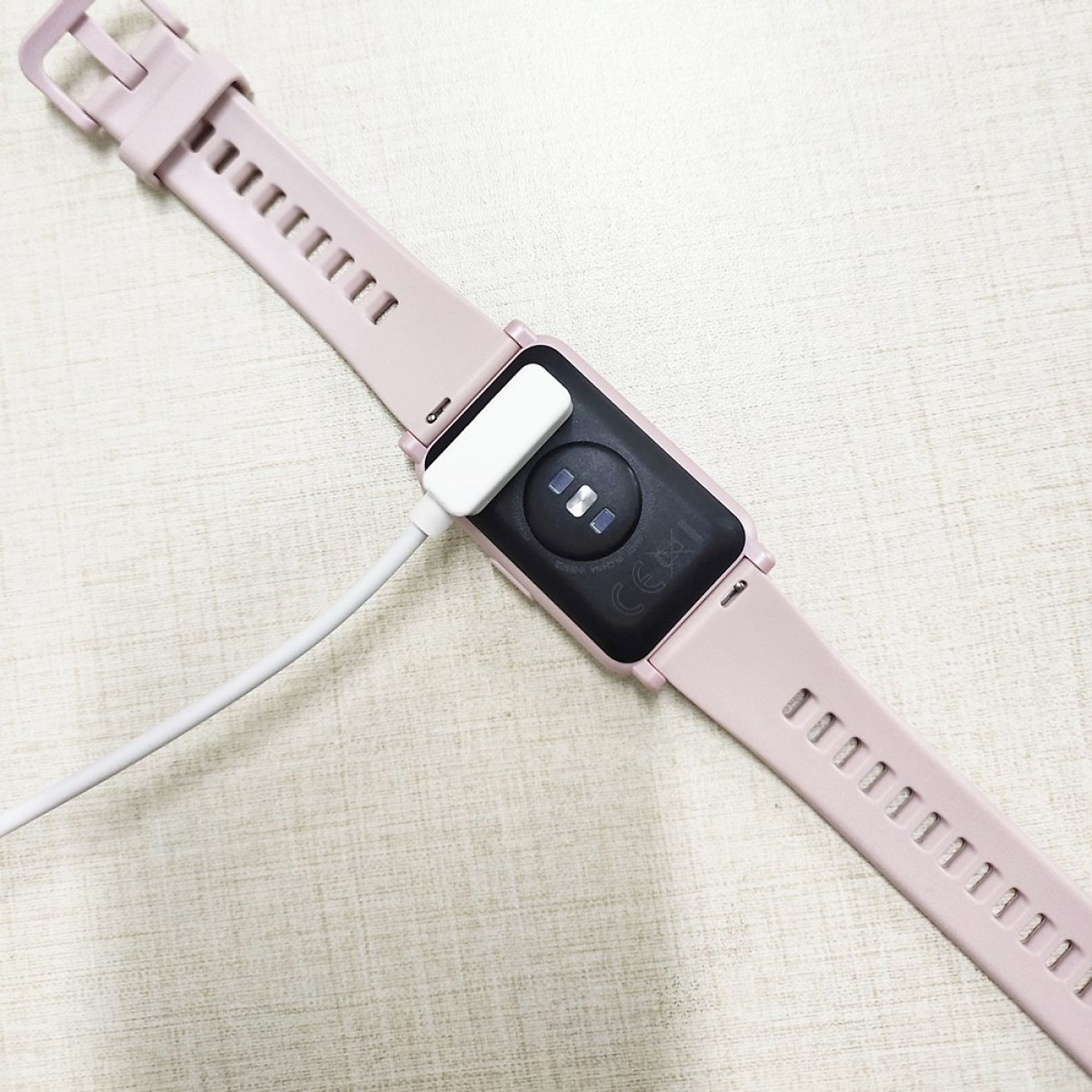 Eine rosa Smartwatch wird aufgeladen. Das Ladegerät ist an der Rückseite der Uhr befestigt.