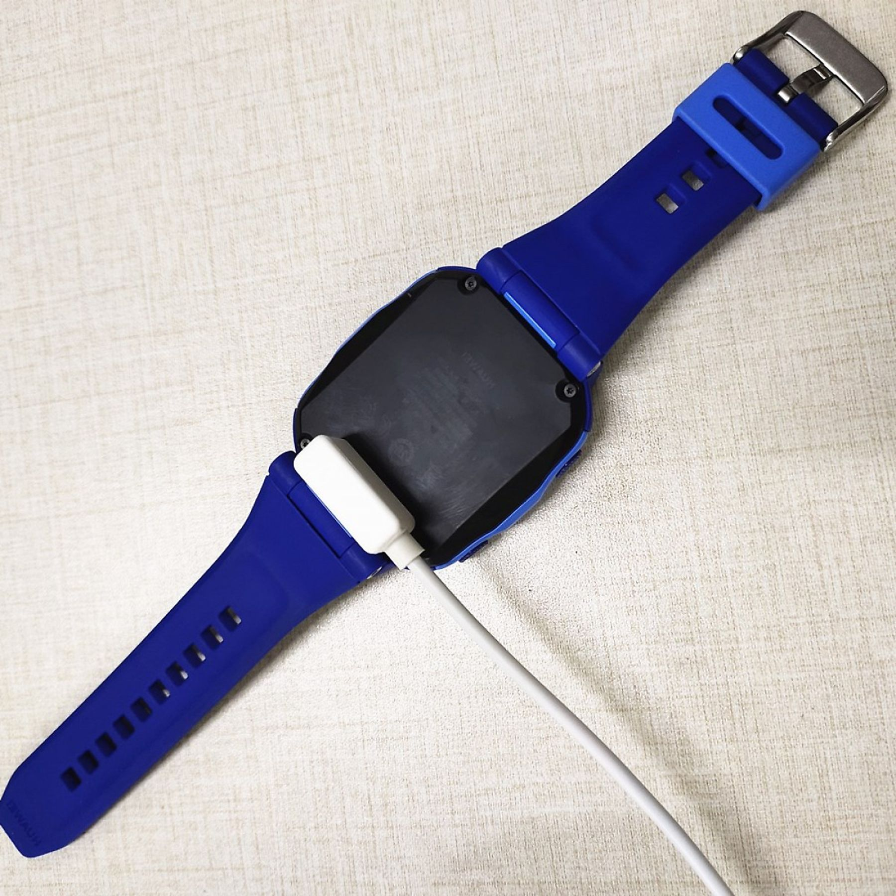 Blaue Smartwatch auf einer Oberfläche, Ladekabel am Handgelenk befestigt, Rückseite sichtbar.