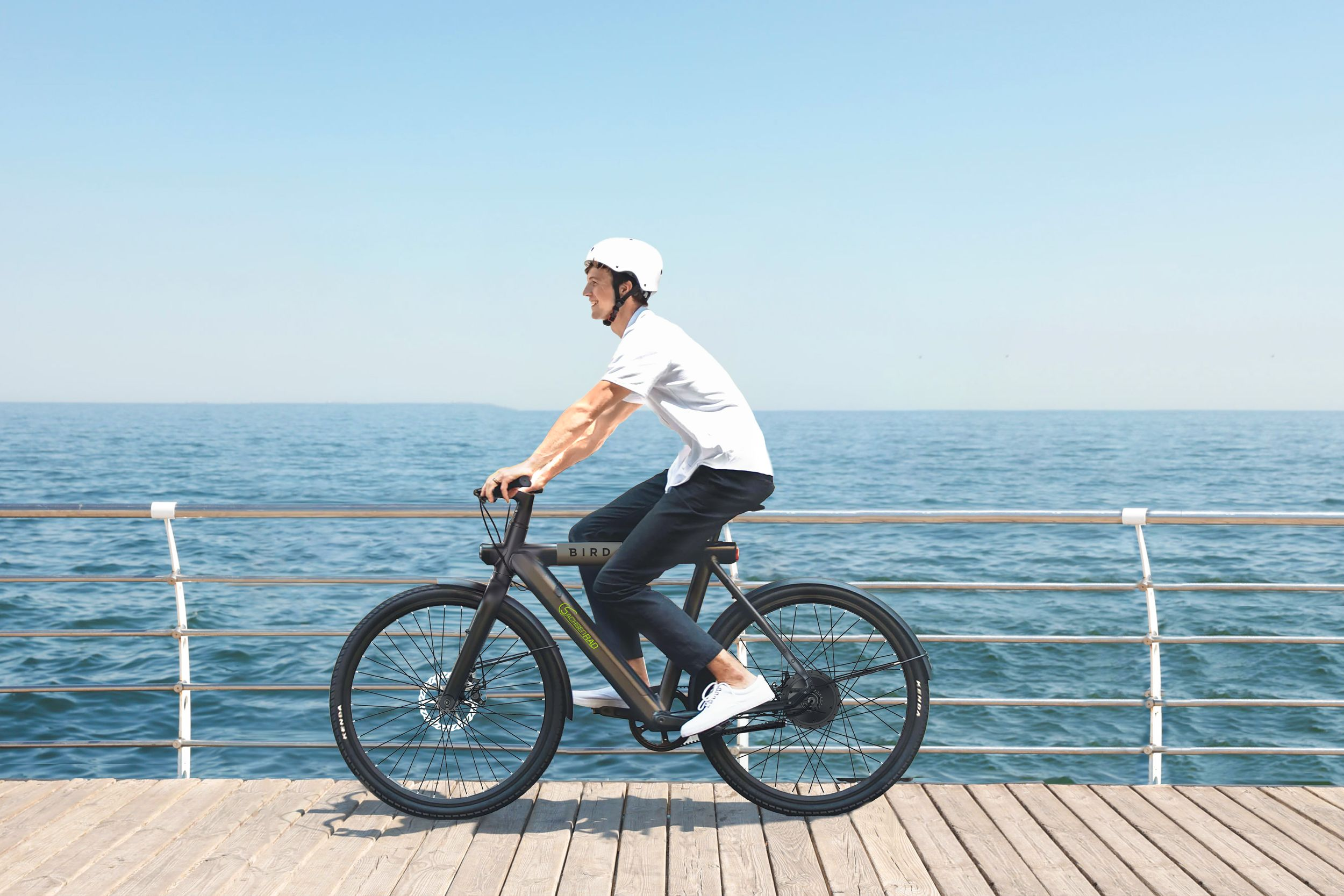 Mann fährt auf einem schwarzen und grünen Fahrrad auf einem Holzsteg am Meer entlang.