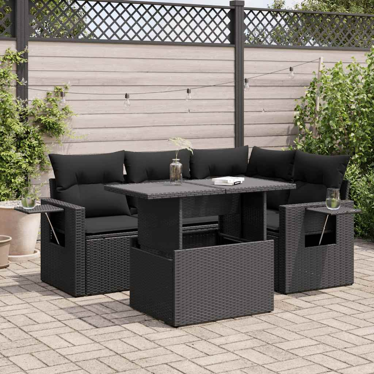 Set di mobili da esterno in vimini nero su un patio pavimentato. Include componibile, tavolo e due sedute.