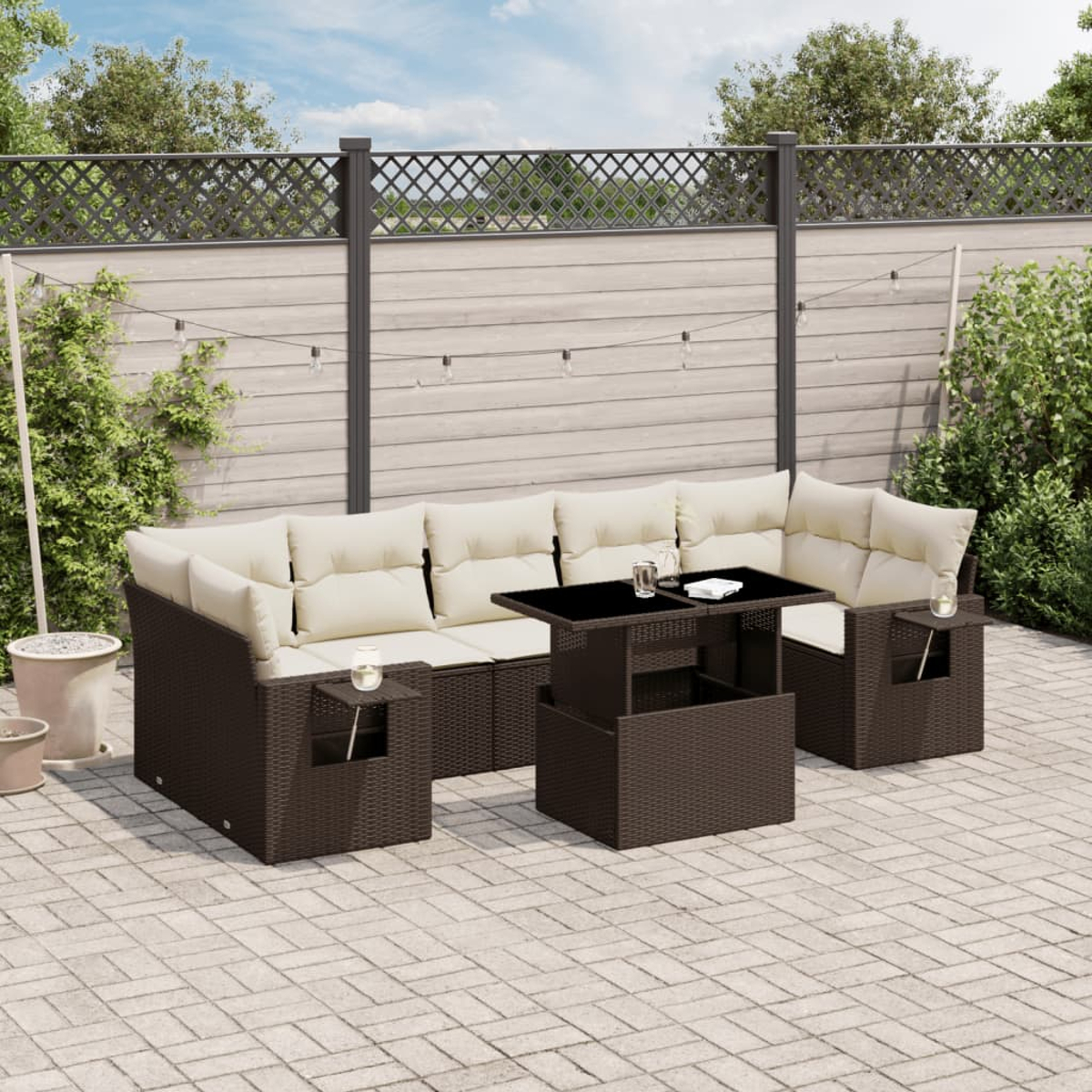 Braunes Outdoor-Geflechtmöbel-Set mit Tisch. Beige Kissen. Hintergrund: Holzzaun, Terrasse und Pflanzen.