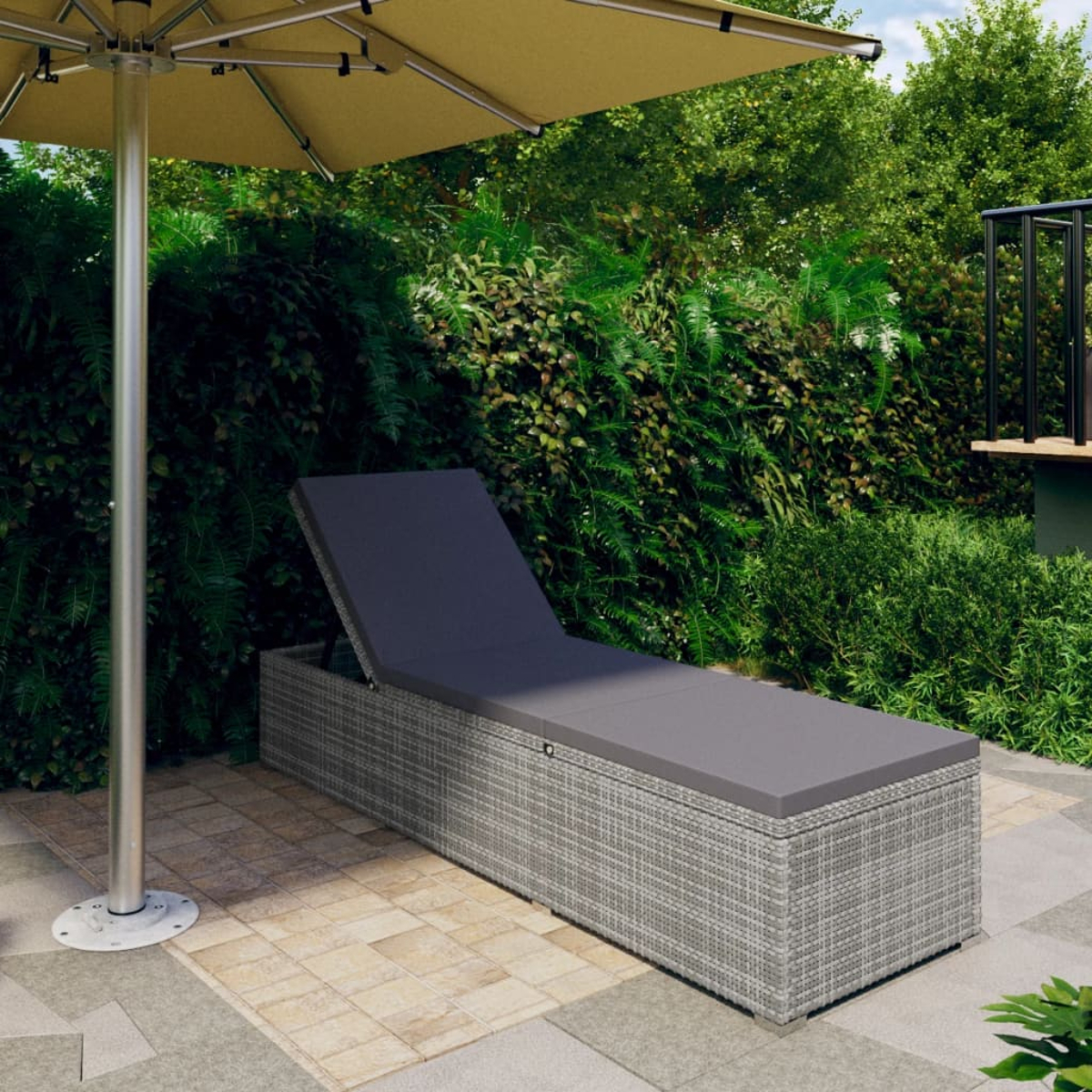Graue Outdoor-Sonnenliege aus Korbgeflecht mit grauem Kissen unter einem gelben Sonnenschirm auf einer Terrasse.