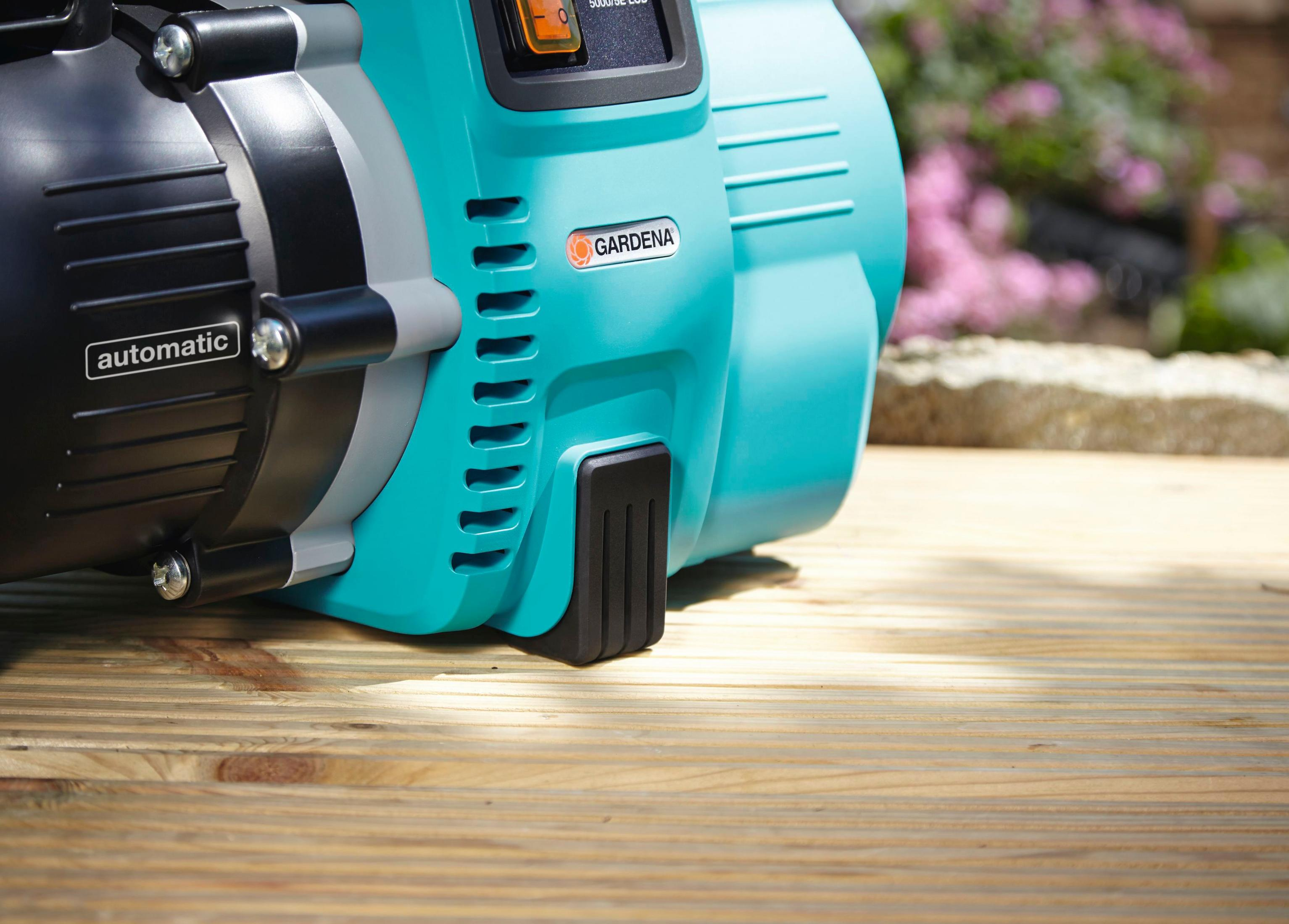 Eine blaue und türkisfarbene automatische Gardena Wasserpumpe auf Holzbohlen.