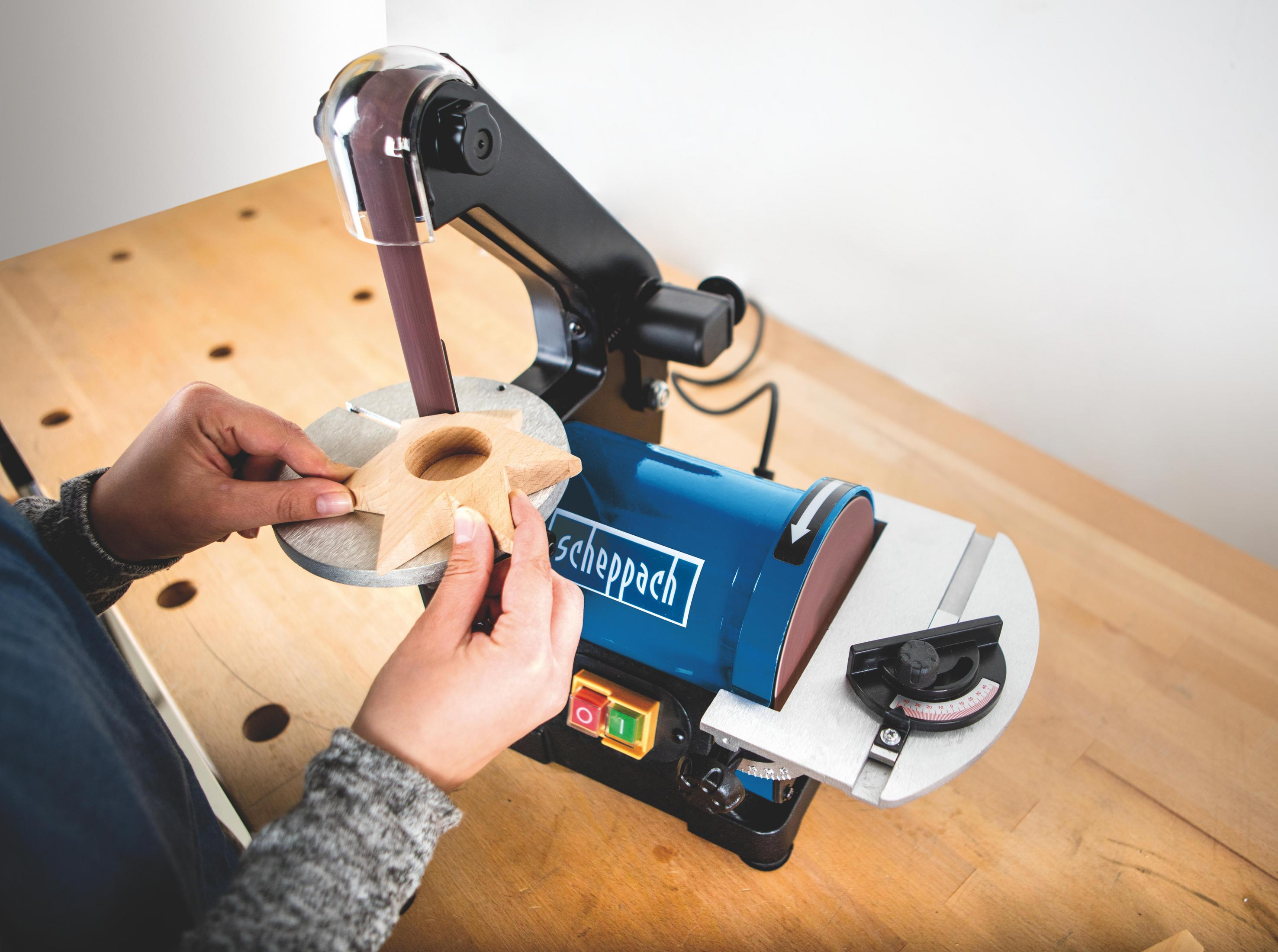 Donna che usa una levigatrice a nastro per modellare una stella di legno. La macchina è blu e nera.