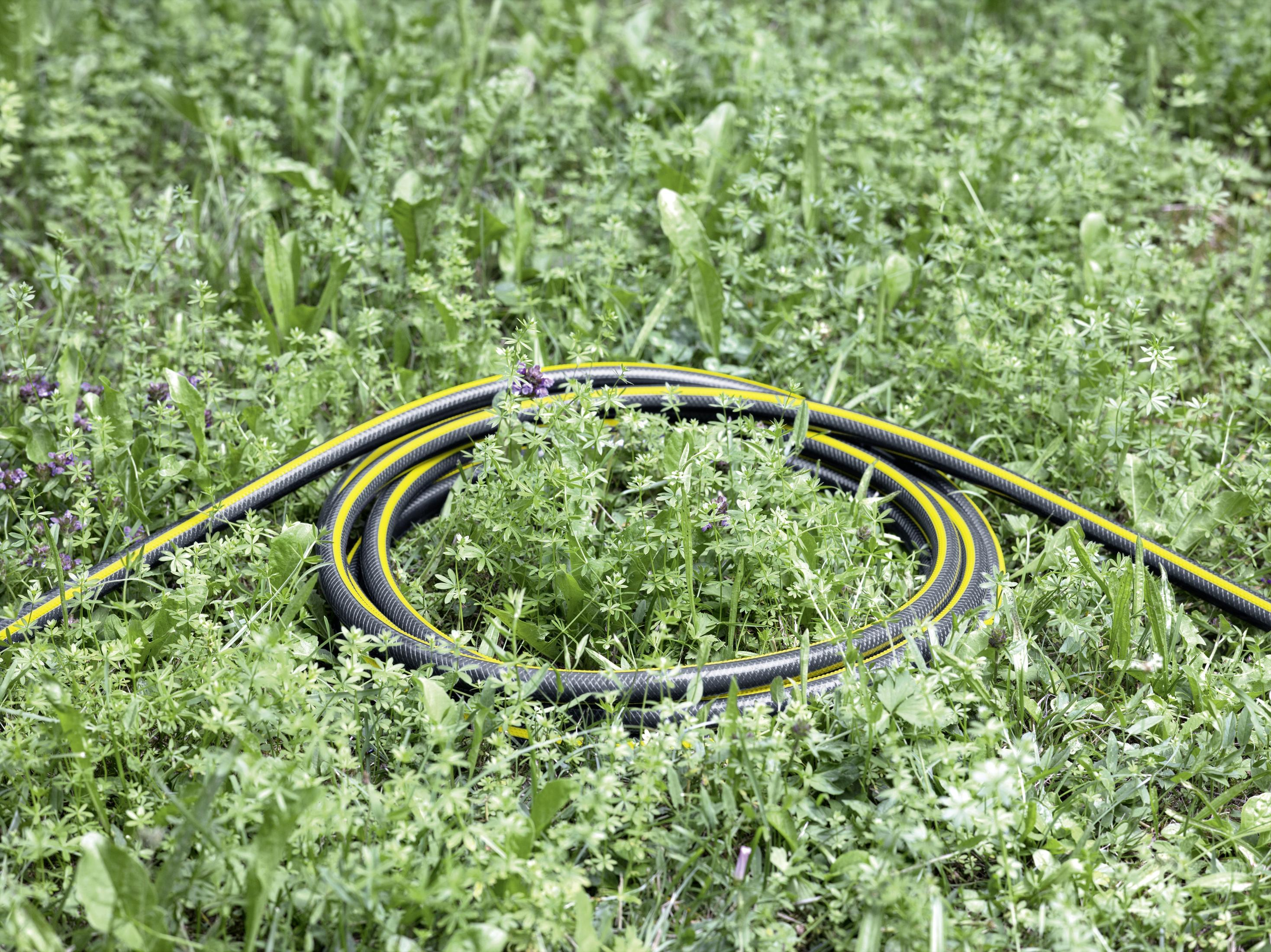 Een opgerolde zwarte en gele tuinslang op een groen grasveld. De slang staat in het midden.