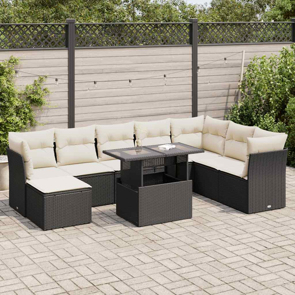 Divano componibile da esterno in vimini grigio scuro con cuscini color crema e tavolo nero, su un patio in mattoni.