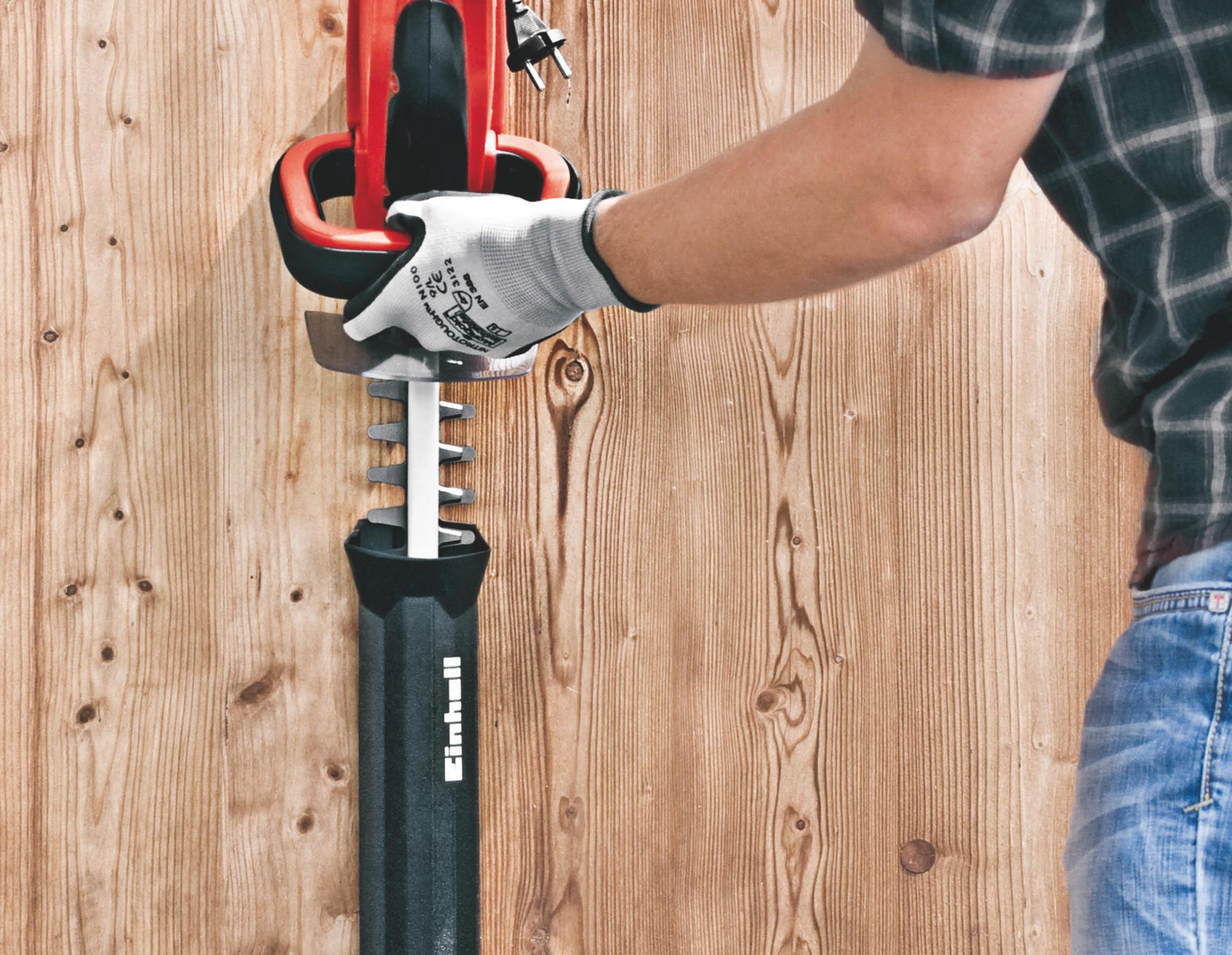 Osoba trzyma czerwono-czarne nożyce do żywopłotu przy drewnianej ścianie.