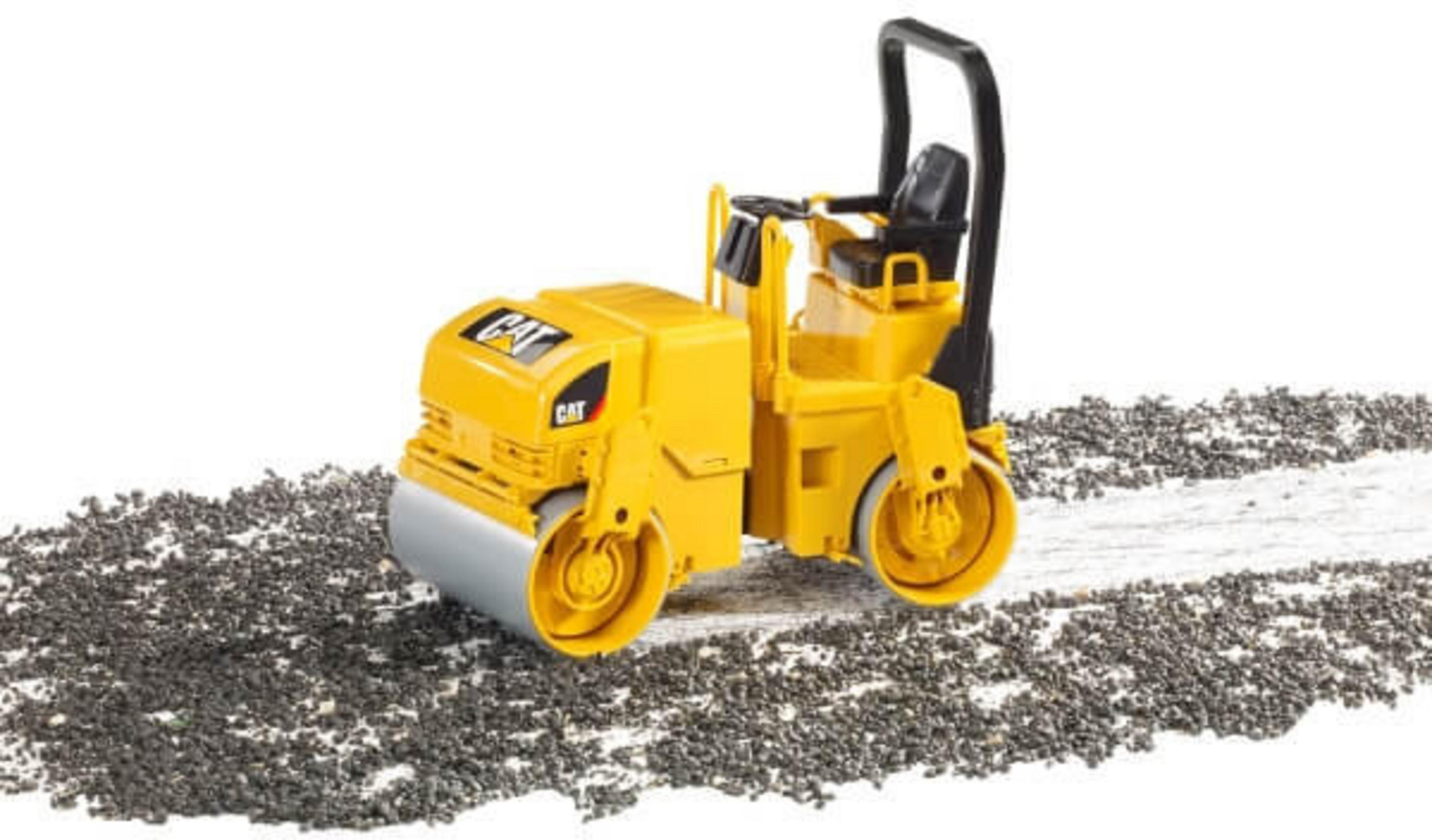 Żółty walec drogowy CAT na białej powierzchni z rozrzuconymi ciemnymi kamykami.