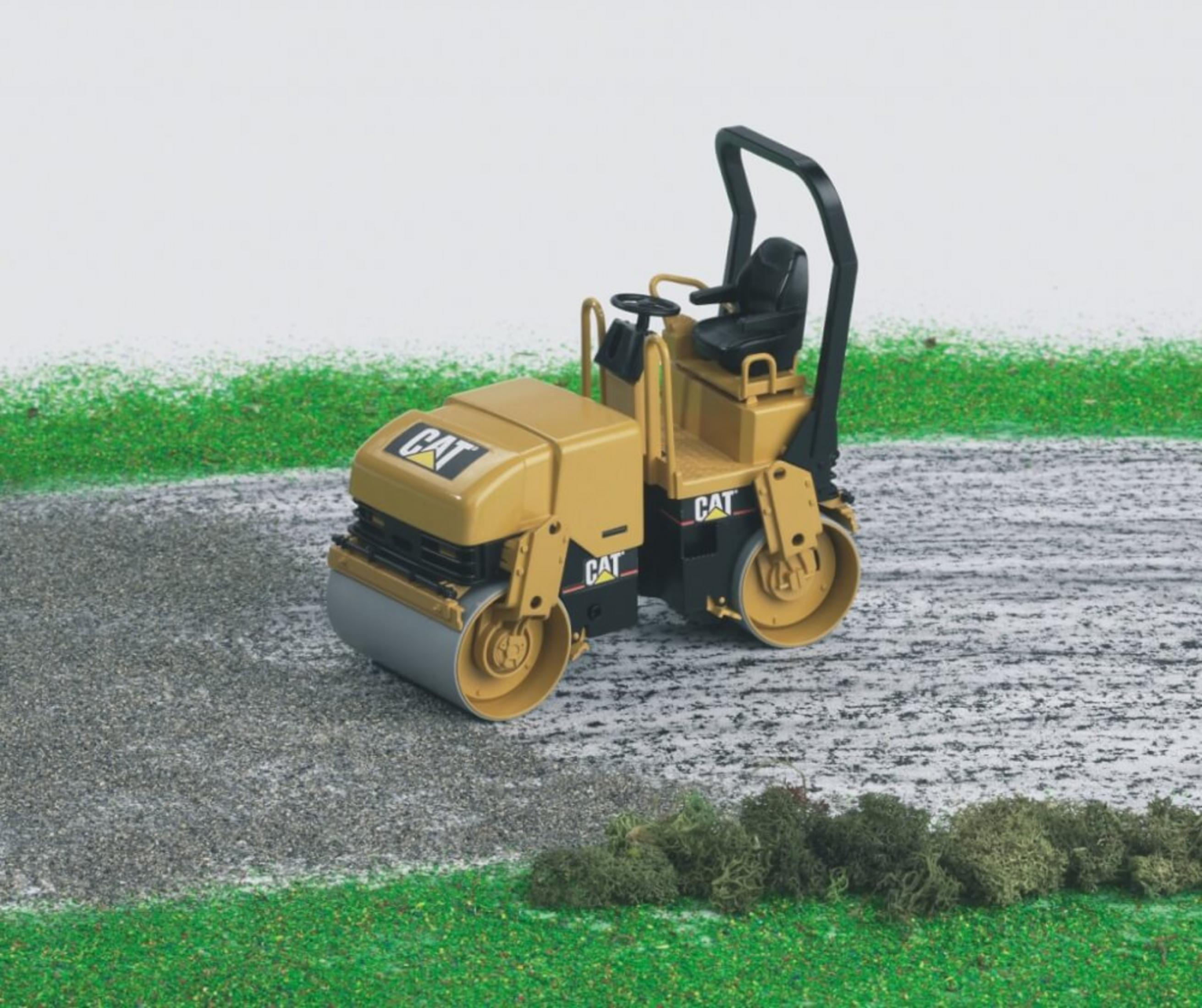 Żółty walec budowlany CAT na utwardzonej drodze z zieloną trawą.