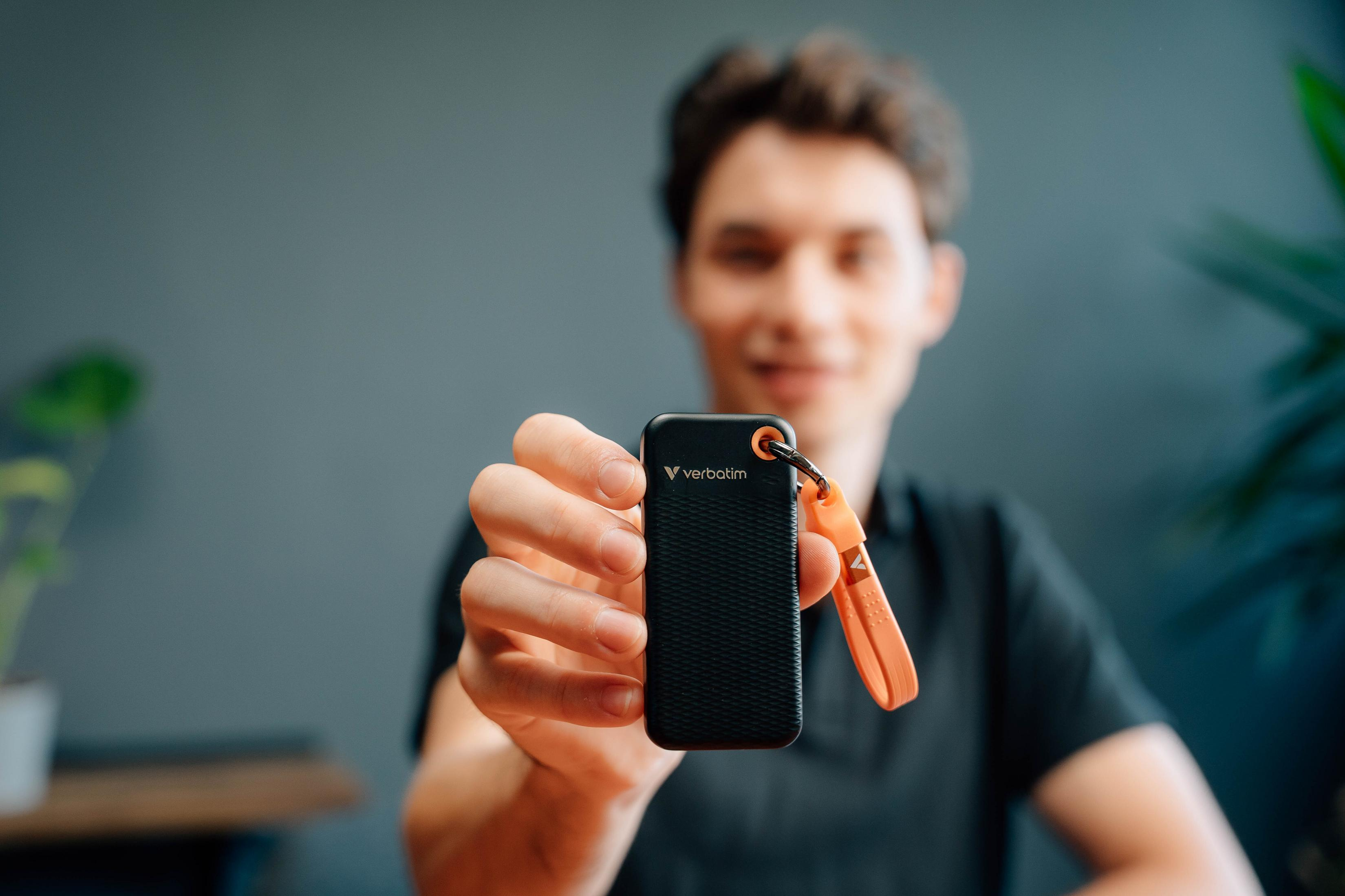 Mężczyzna trzyma czarny dysk SSD Verbatim z pomarańczowym mocowaniem kabla. Rozmyte tło.