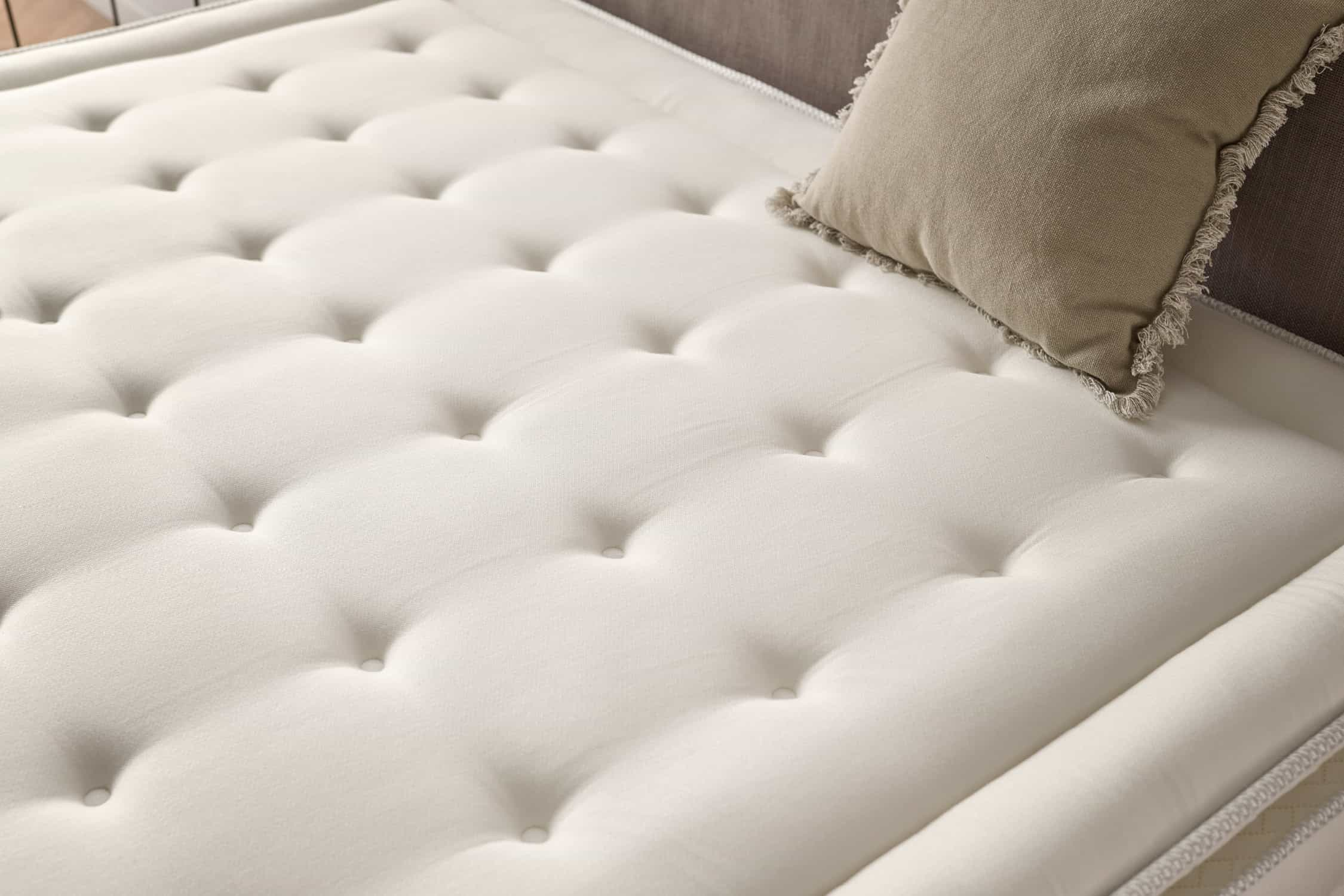 Primer plano de un colchón crema con botones con mechones. Una almohada beige descansa sobre él.