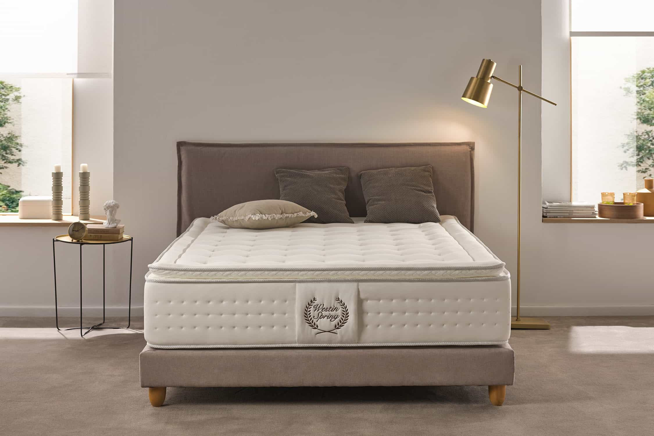 Dormitorio con cama y almohadas. Una lámpara y una mesita de noche están al lado. Ventana al fondo.