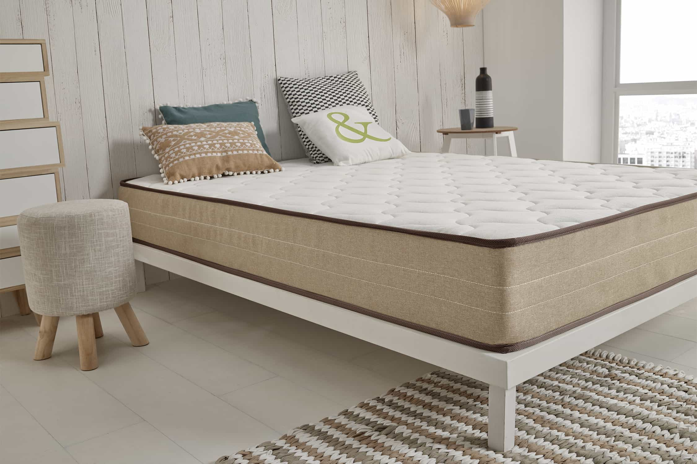 Cama con marco blanco, colchón, almohadas y otros elementos decorativos.