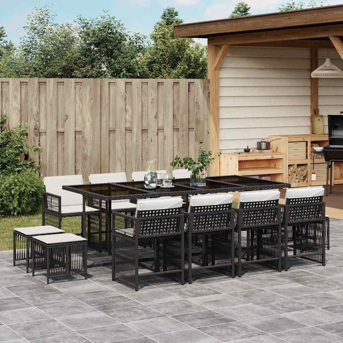 Set da pranzo all'aperto: tavolo con sedie, sgabelli. Il set è su un patio in pietra. Sfondo: recinzione in legno e alberi verdi.
