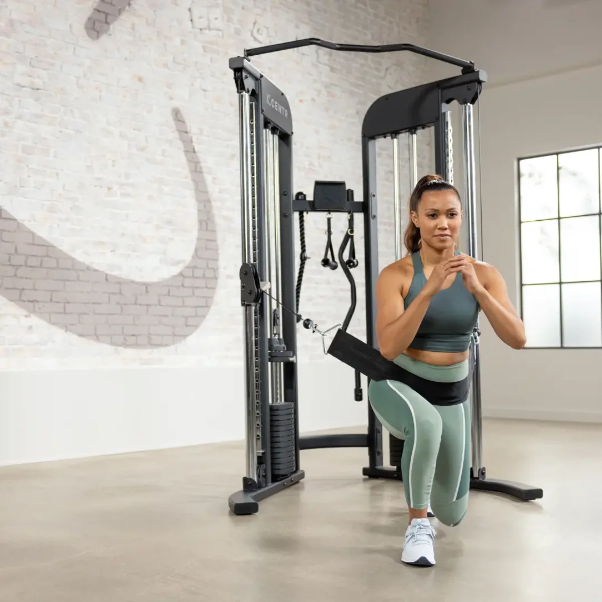 Femme en tenue de sport fait des fentes attachée à une machine à câble dans une salle de sport.