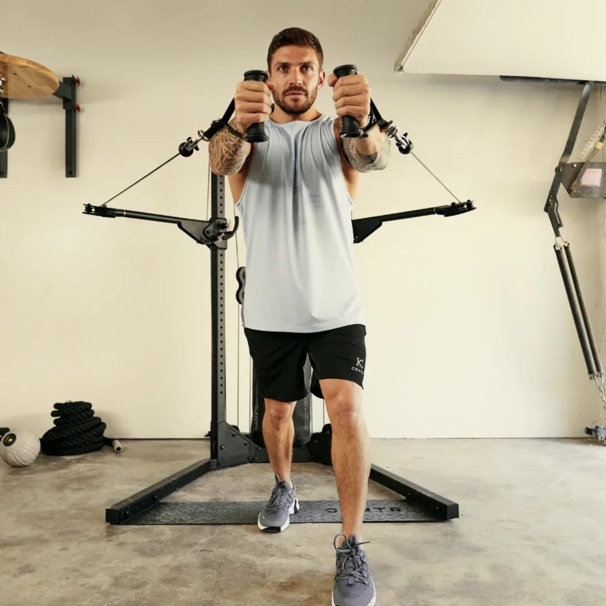 Ein Mann im Fitnessstudio, hält Griffe an einem Kabelzug. Er trägt schwarze Shorts und ein graues Tanktop.