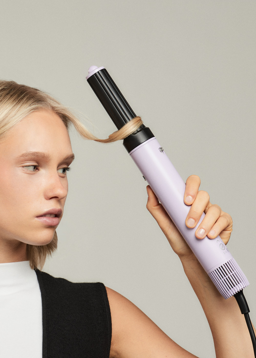 Eine Frau benutzt einen Lockenstab, um ihr Haar zu locken, mit neutralem Hintergrund.