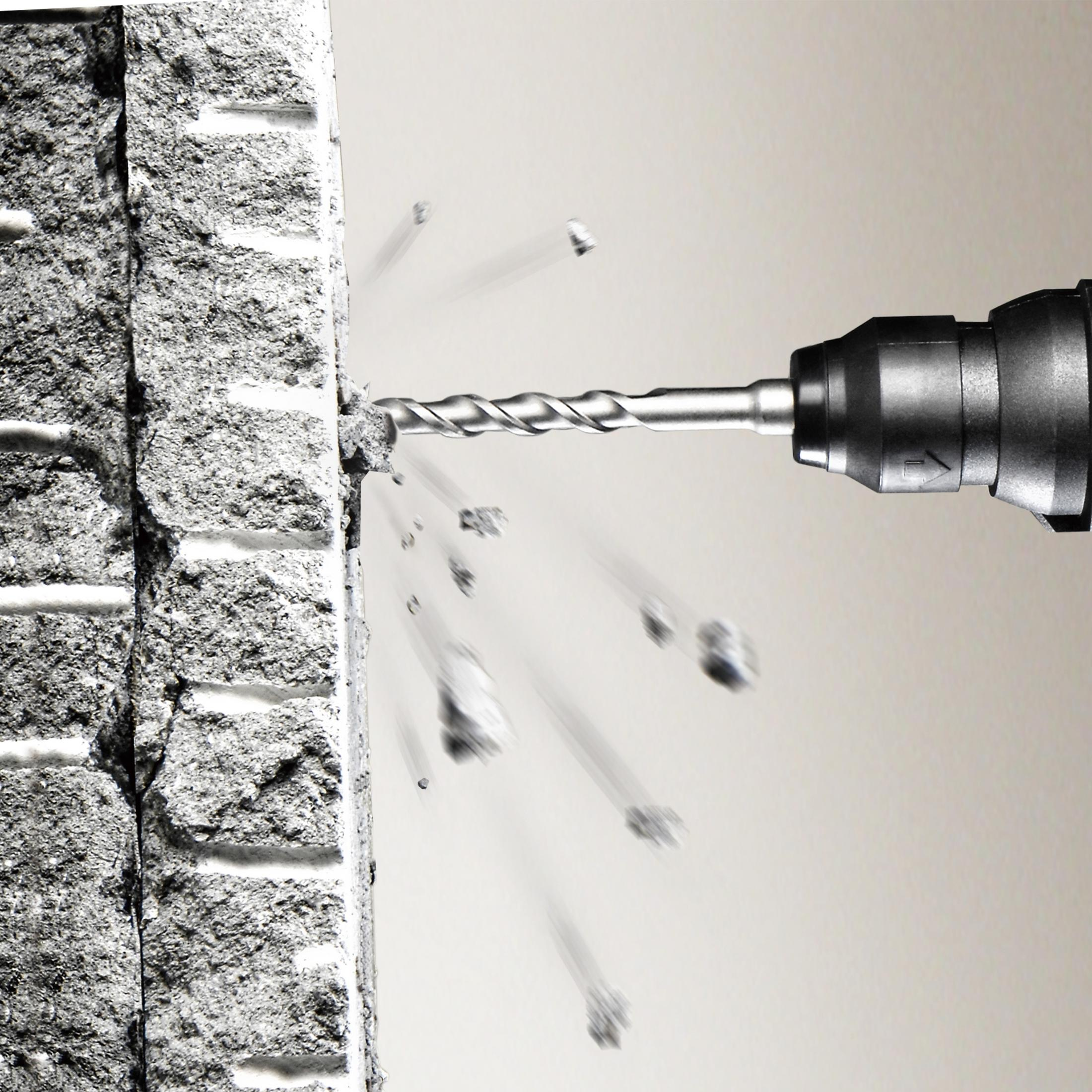Wiertło wiercące w betonowej ścianie. Odłamki wylatują na zewnątrz. Białe tło.