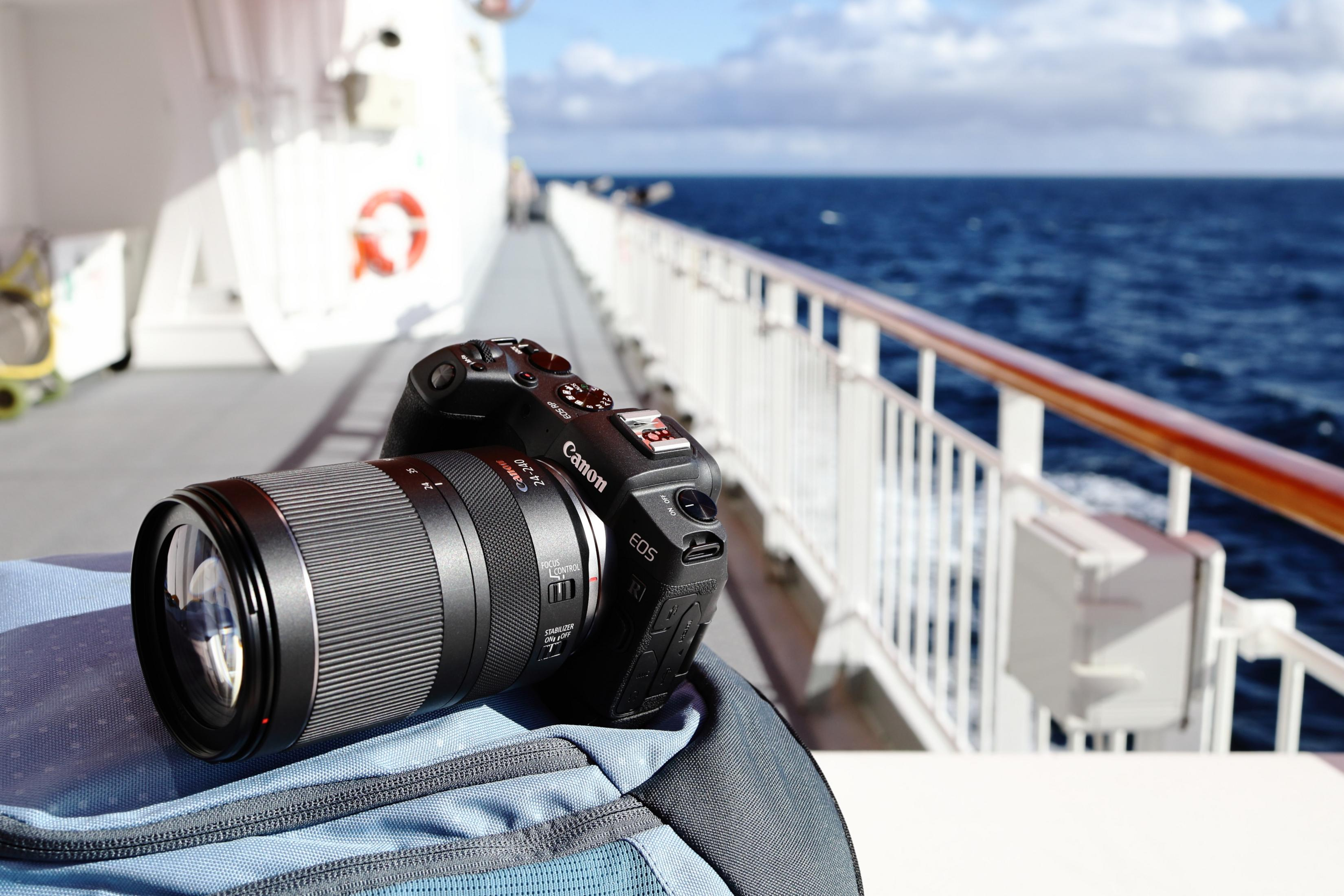 Canon camera on a boat deck, blue water and sky in the background. Focus is on the camera.