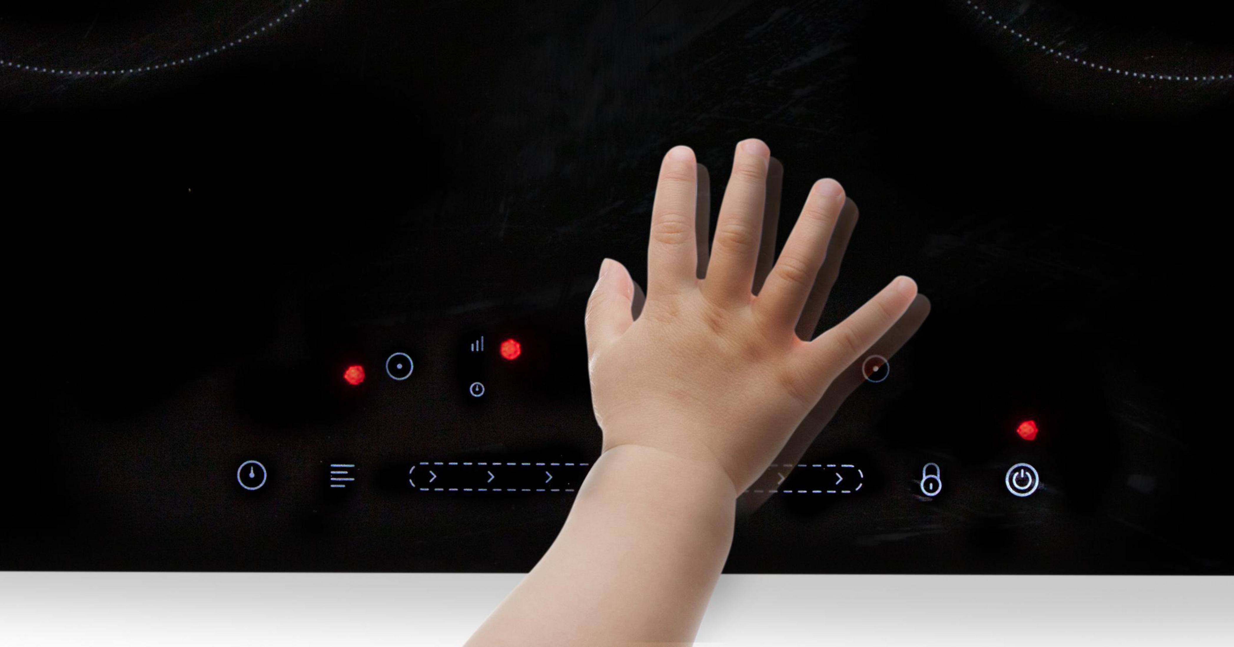 Main d'enfant touchant une plaque à induction noire. Lumières rouges allumées. Fond blanc.