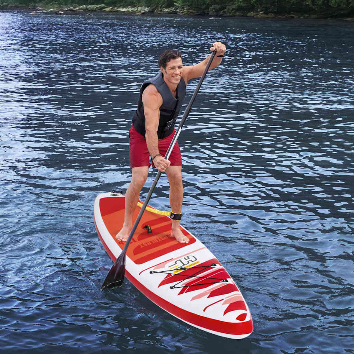 Man paddles a red and white paddleboard on water, wearing a vest and shorts.