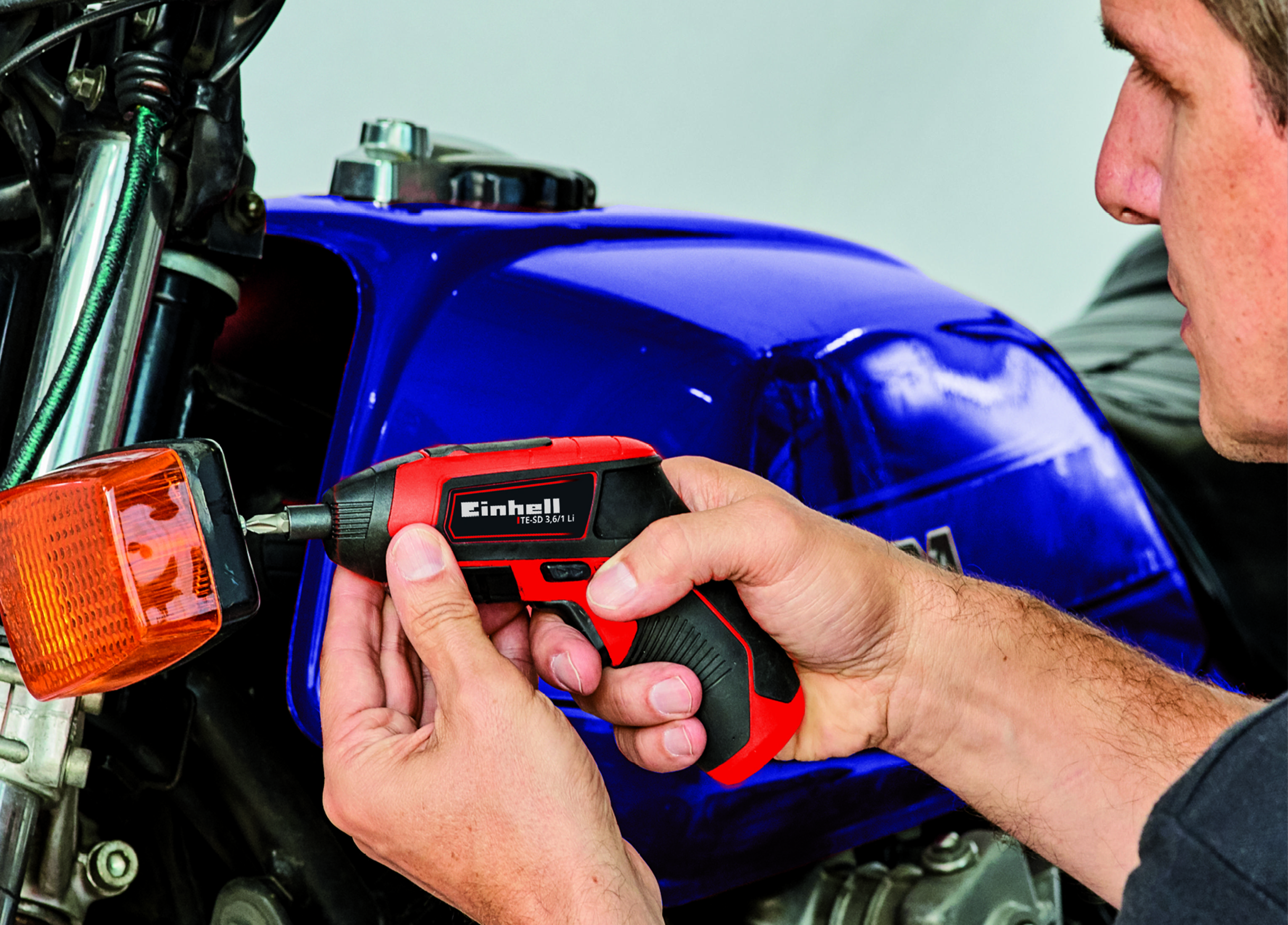Mężczyzna używający czerwono-czarnej wkrętarki akumulatorowej na motocyklu.