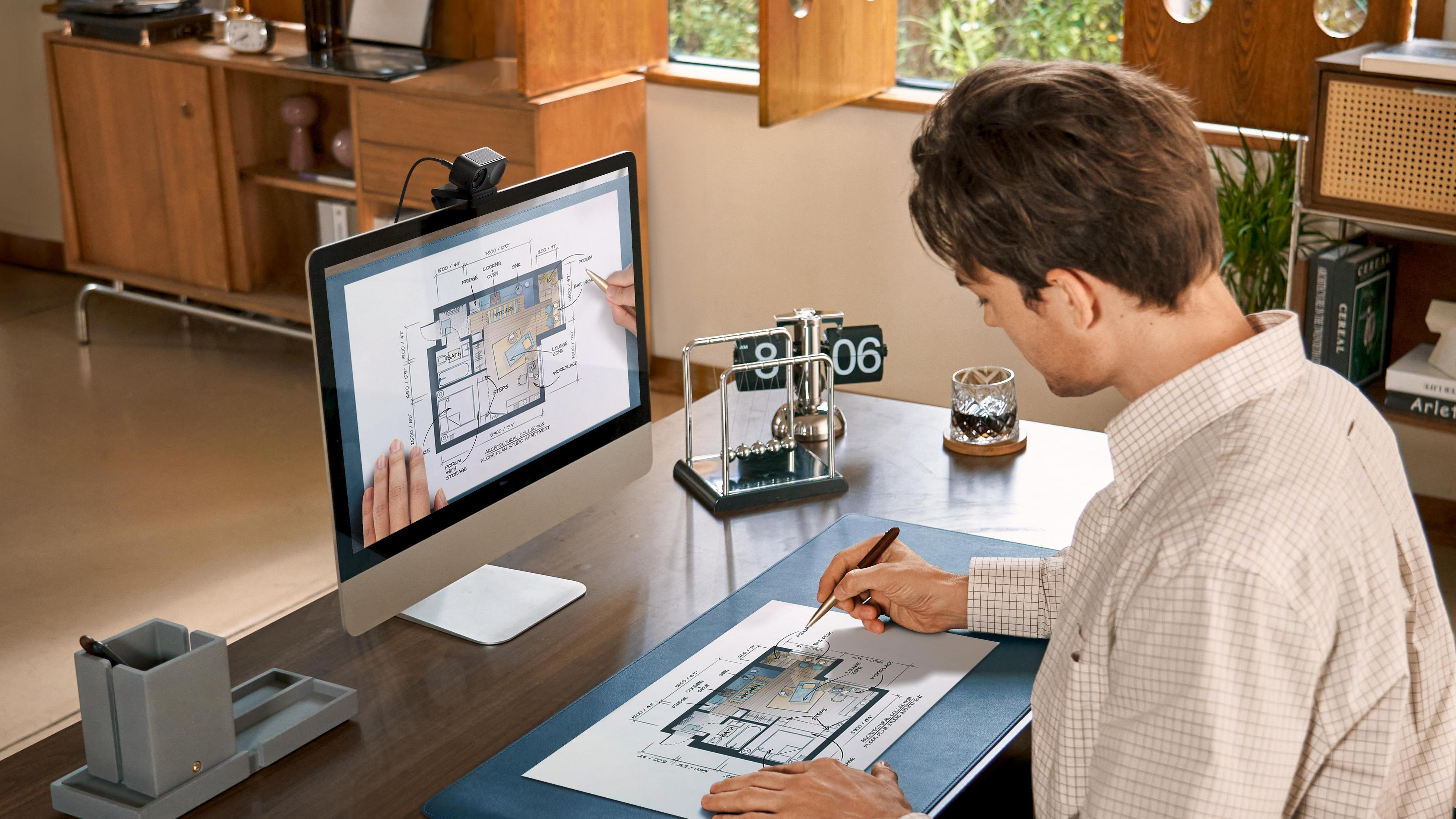 Mężczyzna pracuje na ekranie komputera i papierze, używając pióra.