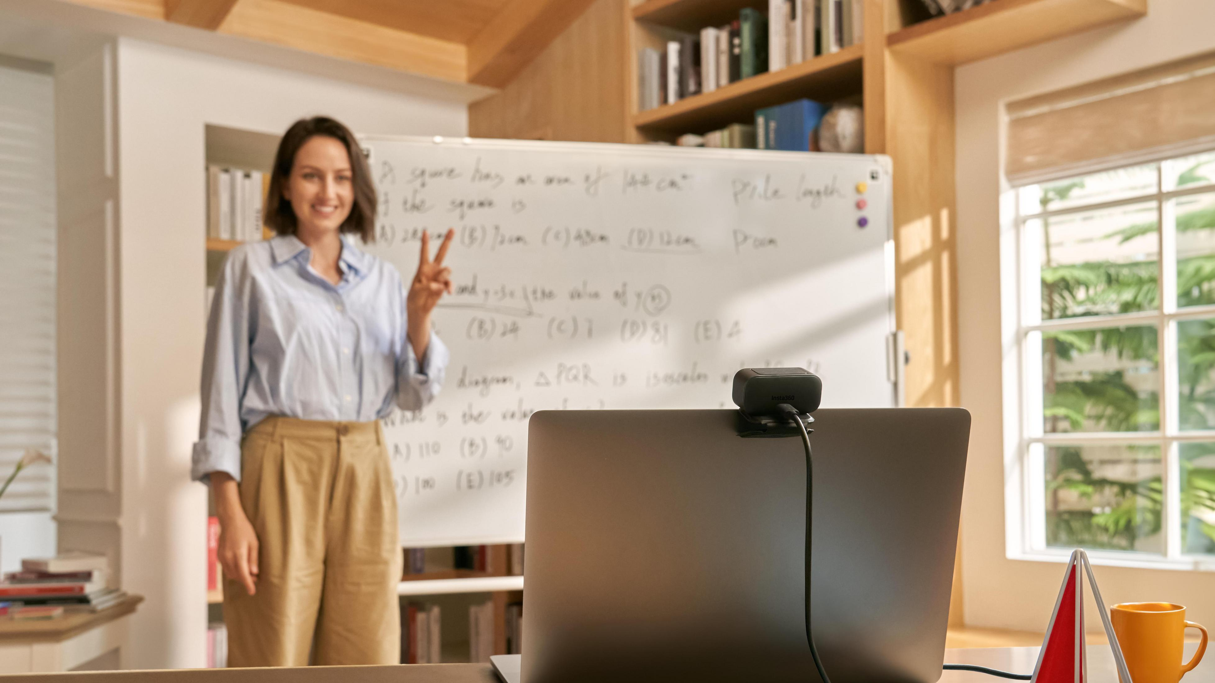 Nauczyciel pokazuje ekran laptopa z tablicą w tle.