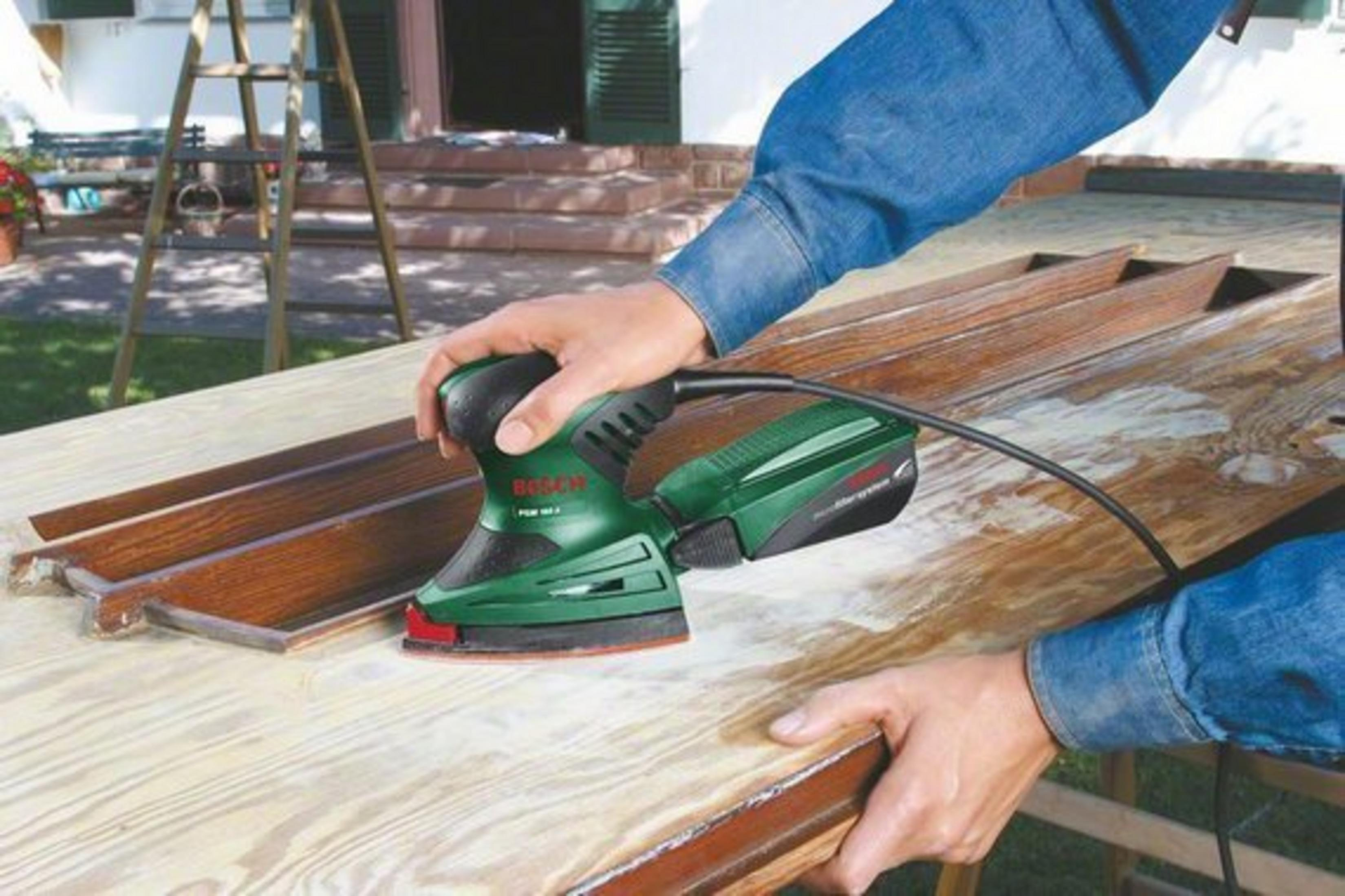 Une personne utilisant une ponceuse verte et noire sur du bois. Le bois est brun clair.