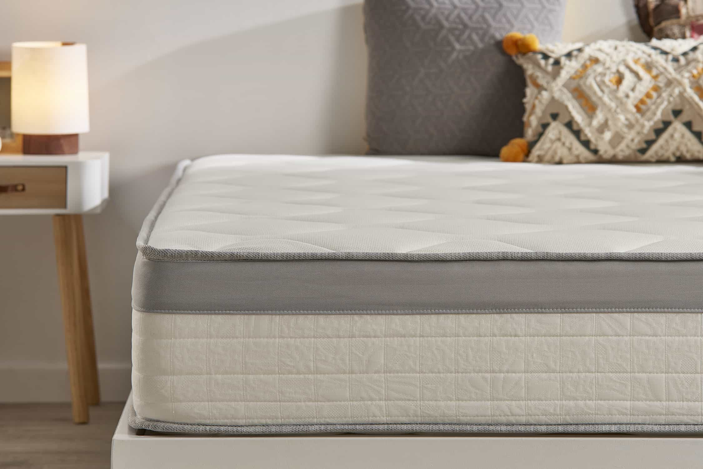Colchón en marco de cama. Almohadas en la cama. Pared blanca y mesa con lámpara.