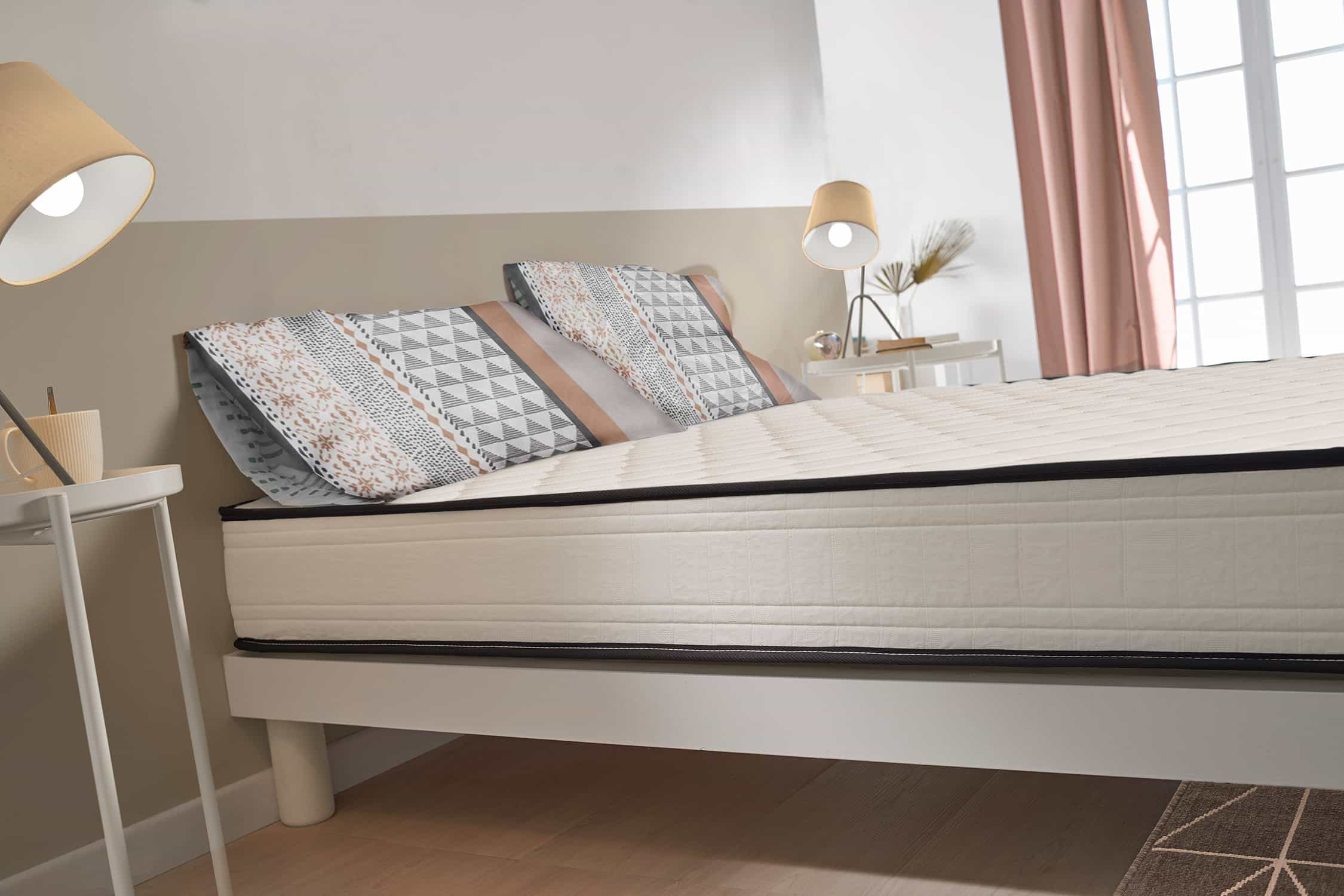 Cama con colchón y almohadas. Dos lámparas en mesitas, cortina al fondo.