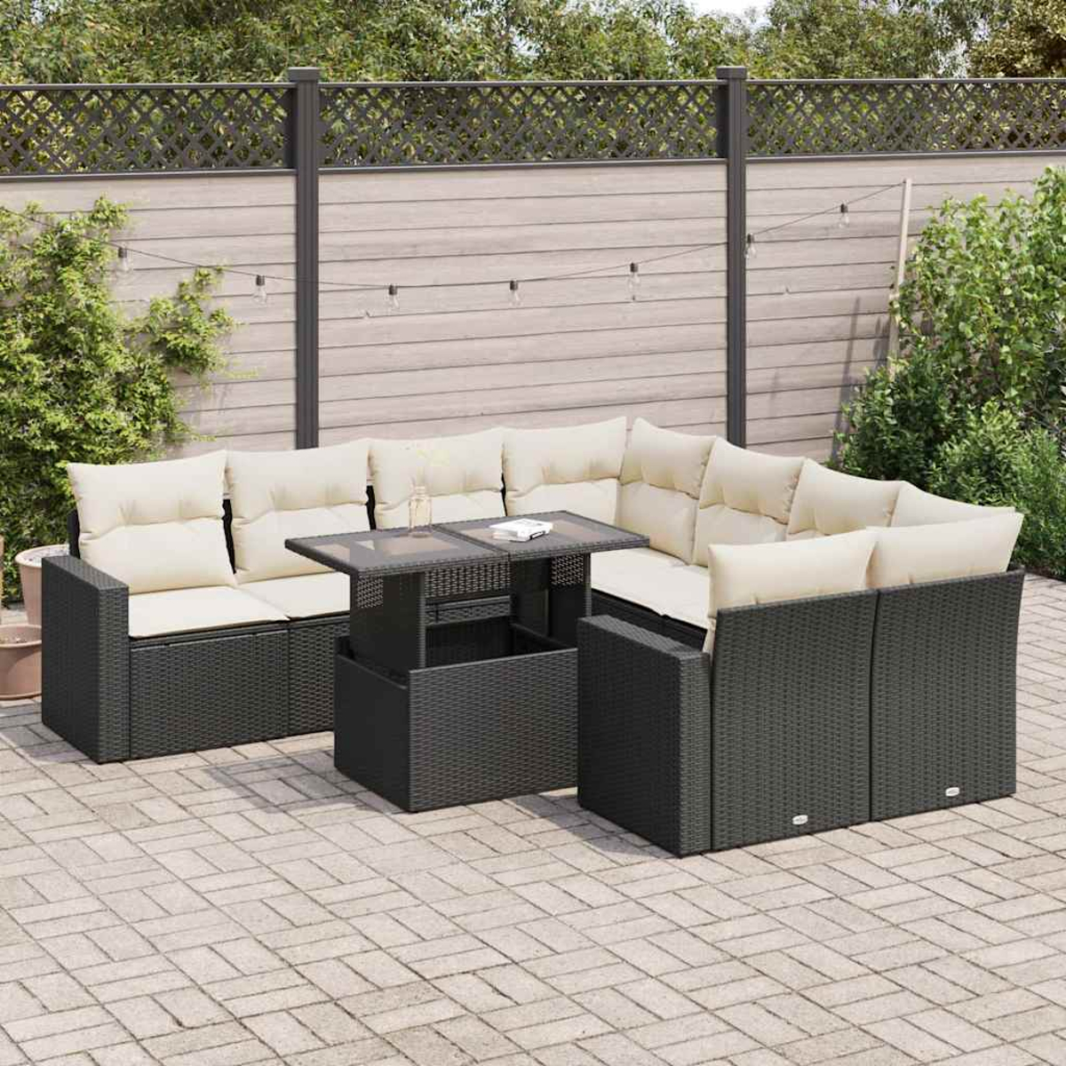 Divano componibile da esterno su un patio con tavolo. Cuscini beige, vimini nero. Sfondo verde.