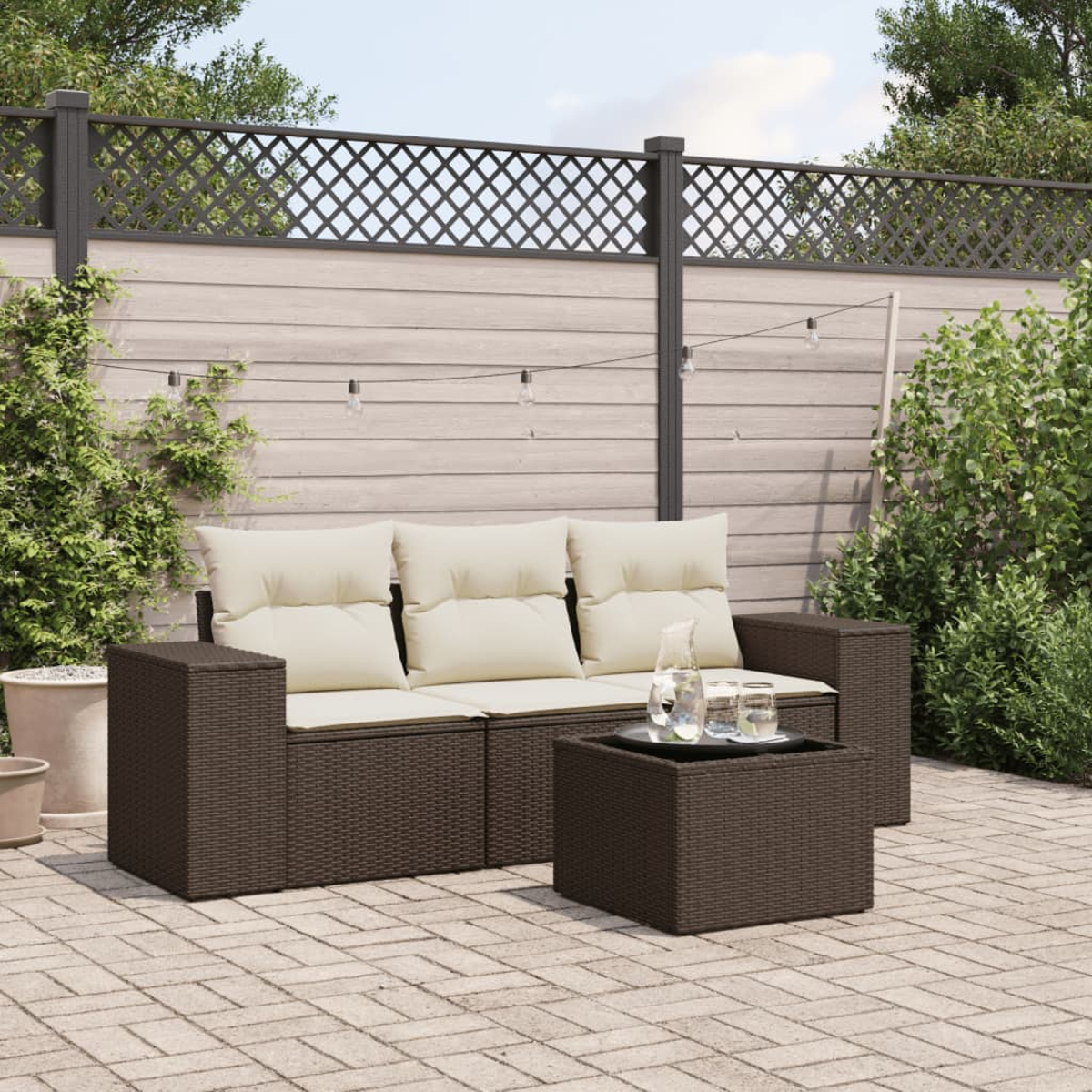 Set di divani in vimini marrone con cuscini color crema e tavolo nero. La scena è su un patio in mattoni.