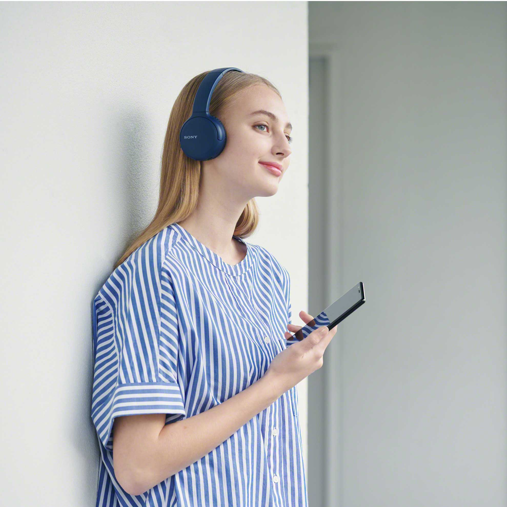Mujer rubia con auriculares azules y camisa a rayas, sosteniendo un teléfono.