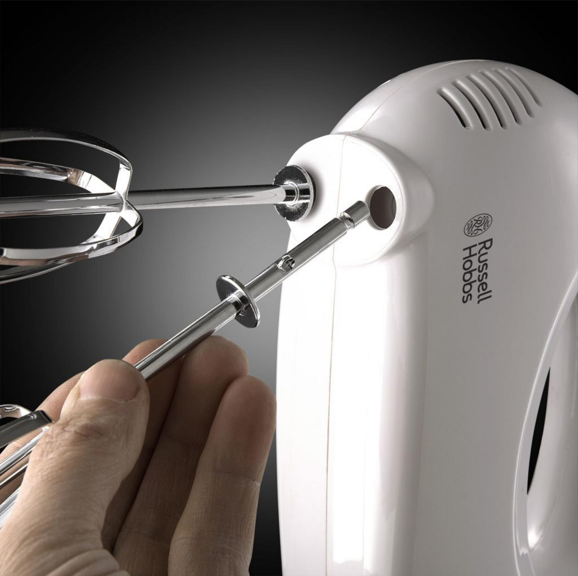 Hand, die einen Schläger in einen weißen Russell Hobbs Handmixer einführt. Nahaufnahme des Mixers und des Aufsatzes.