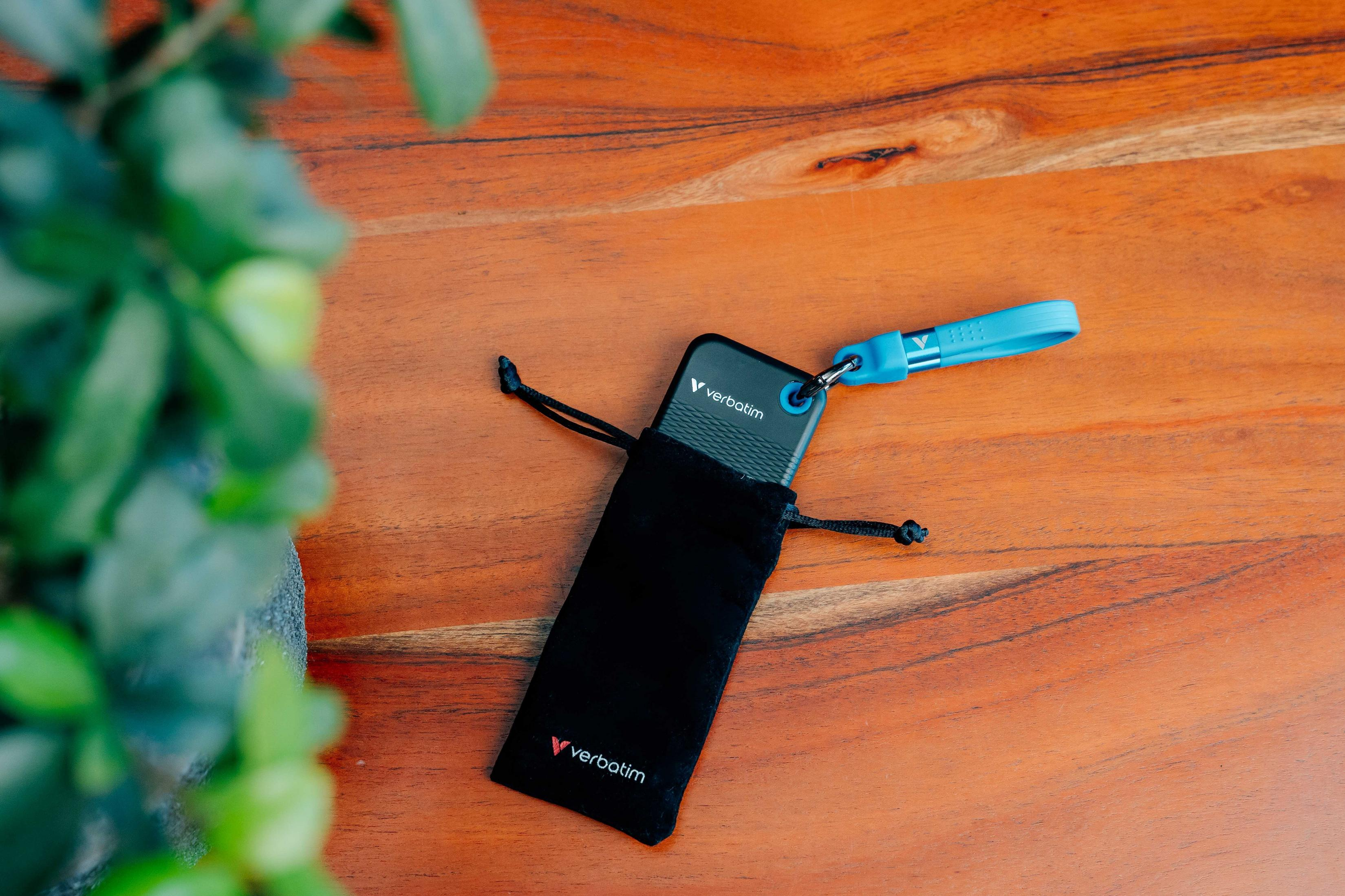 Czarne urządzenie Verbatim w etui na drewnianej powierzchni z niebieską smyczą.