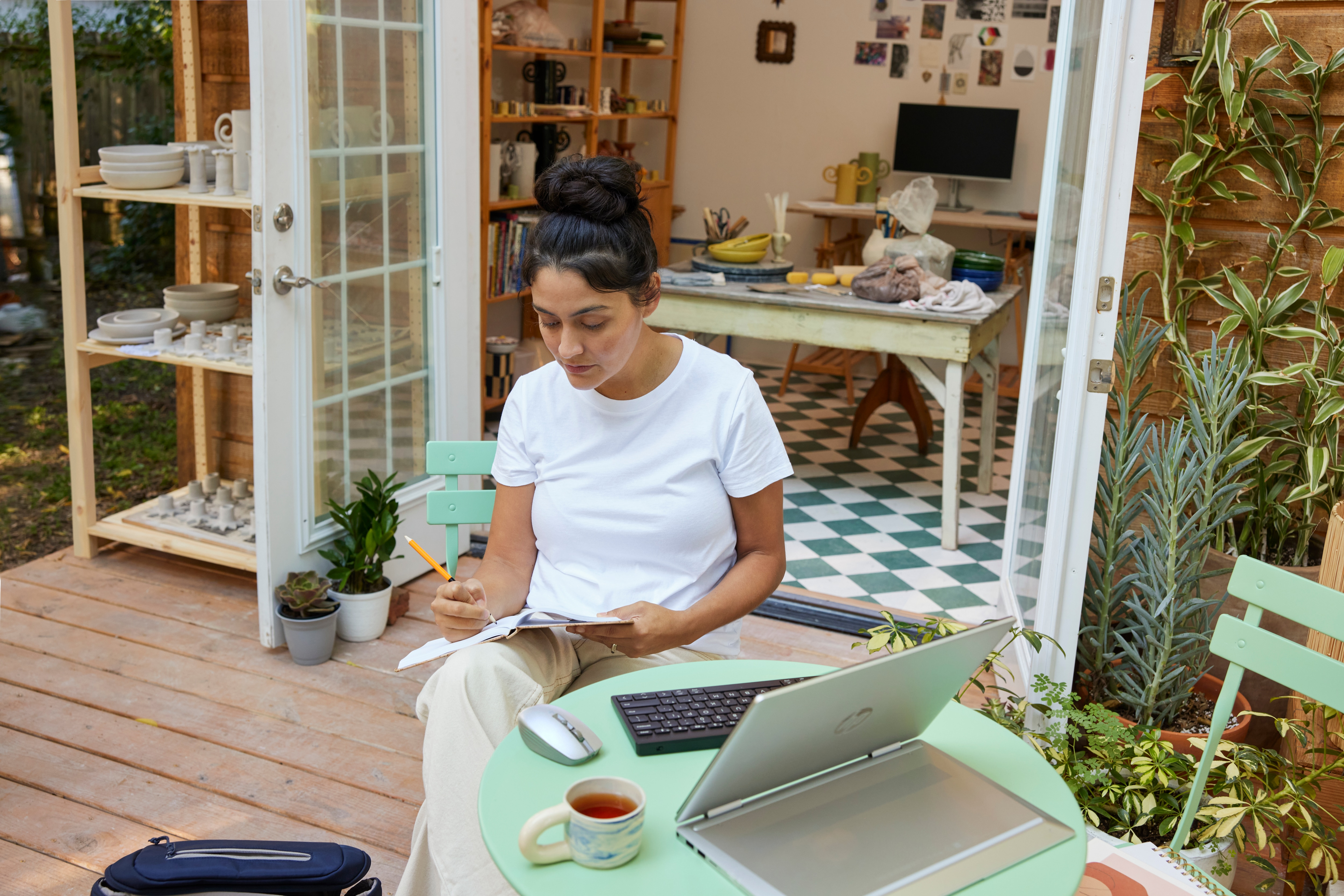 Kobieta pracuje na laptopie na zewnątrz, otoczona roślinami i spokojnym otoczeniem.