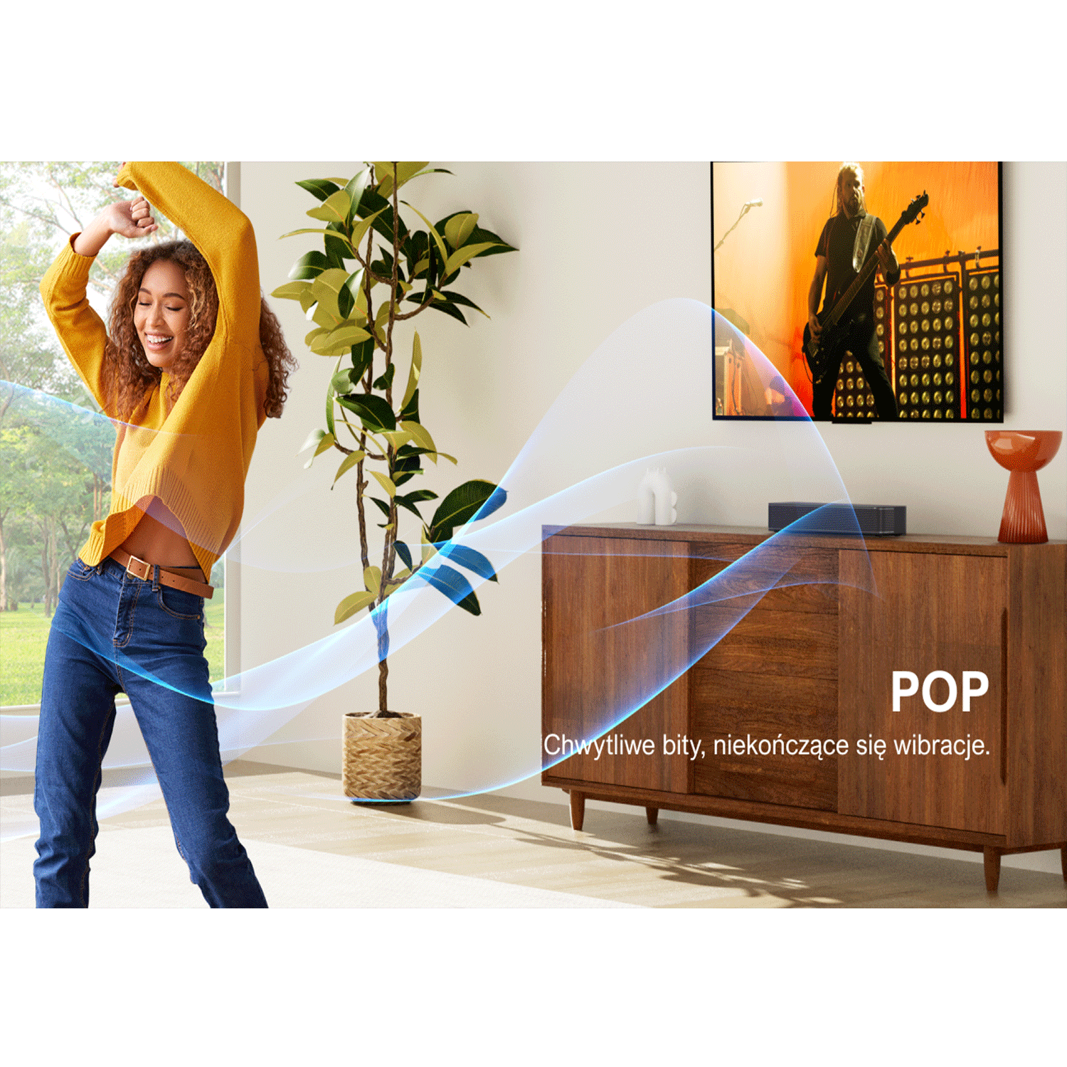 Kobieta tańczy w salonie. TV pokazuje koncert. Drewniana szafka z soundbarem i rośliną. Tekst Pop.