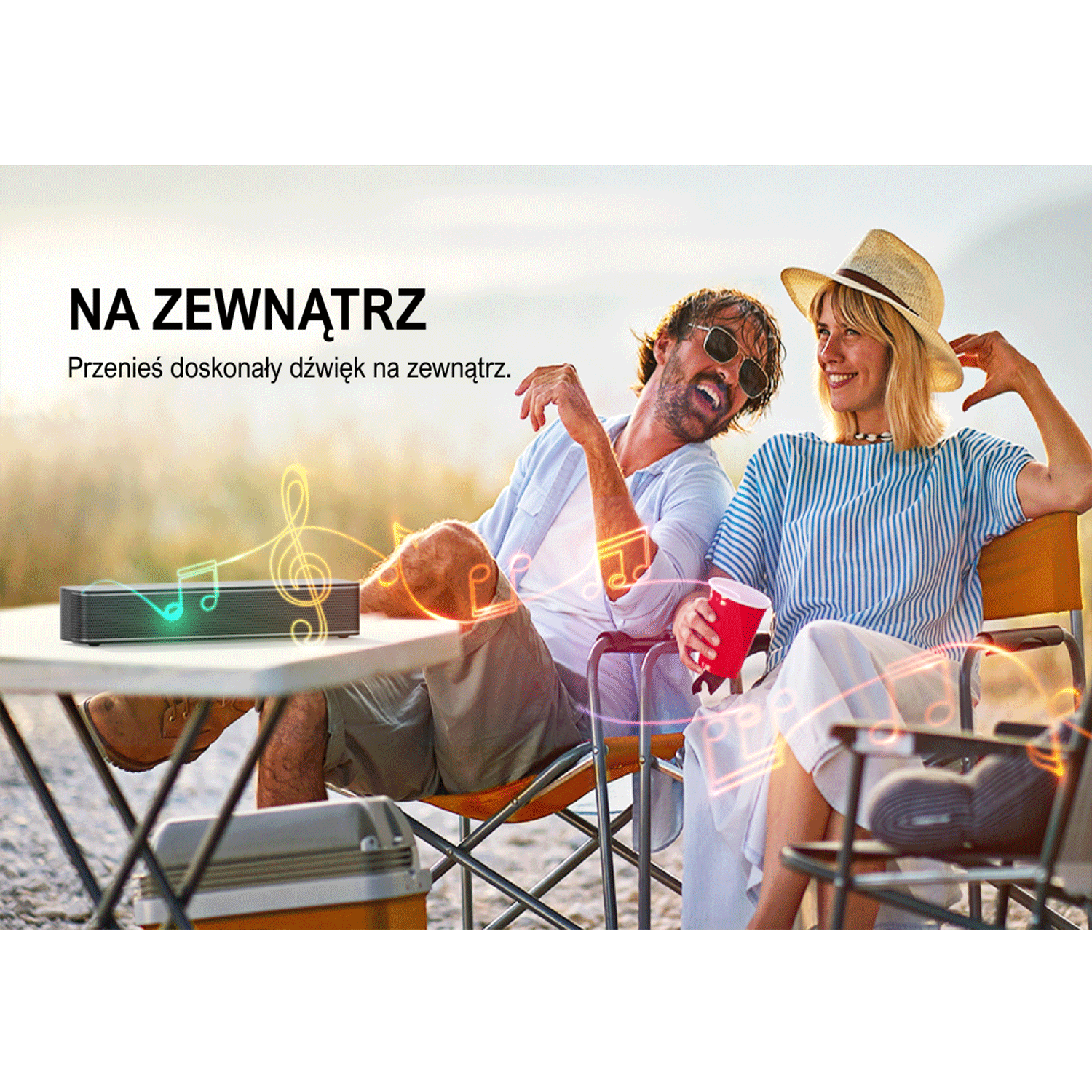 Para na zewnątrz z głośnikiem. Mężczyzna w okularach i kobieta w kapeluszu. Widoczne nuty.