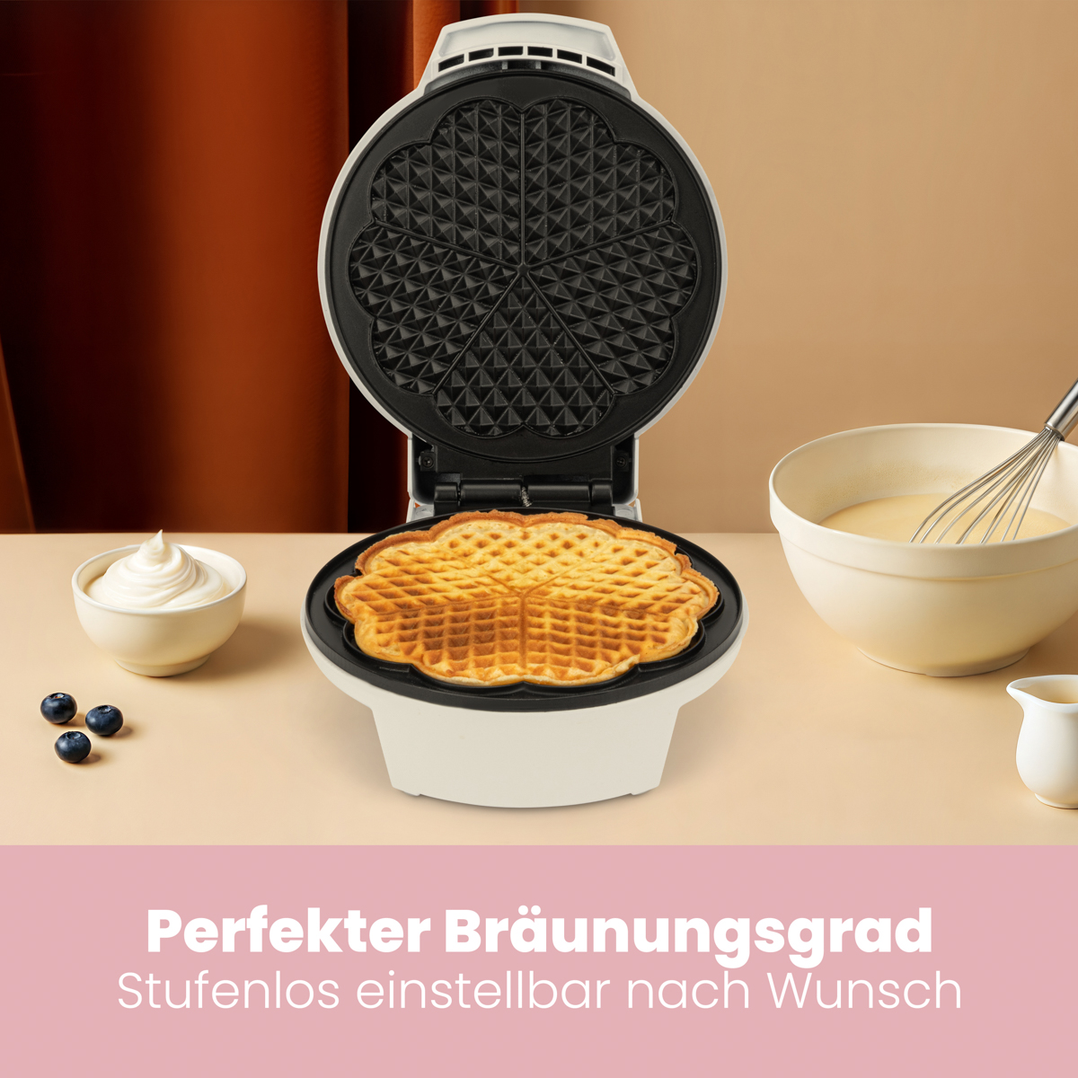 Gofrownica z upieczonym gofrem w środku. Miski z kremem, ciastem i jagodami na stole.