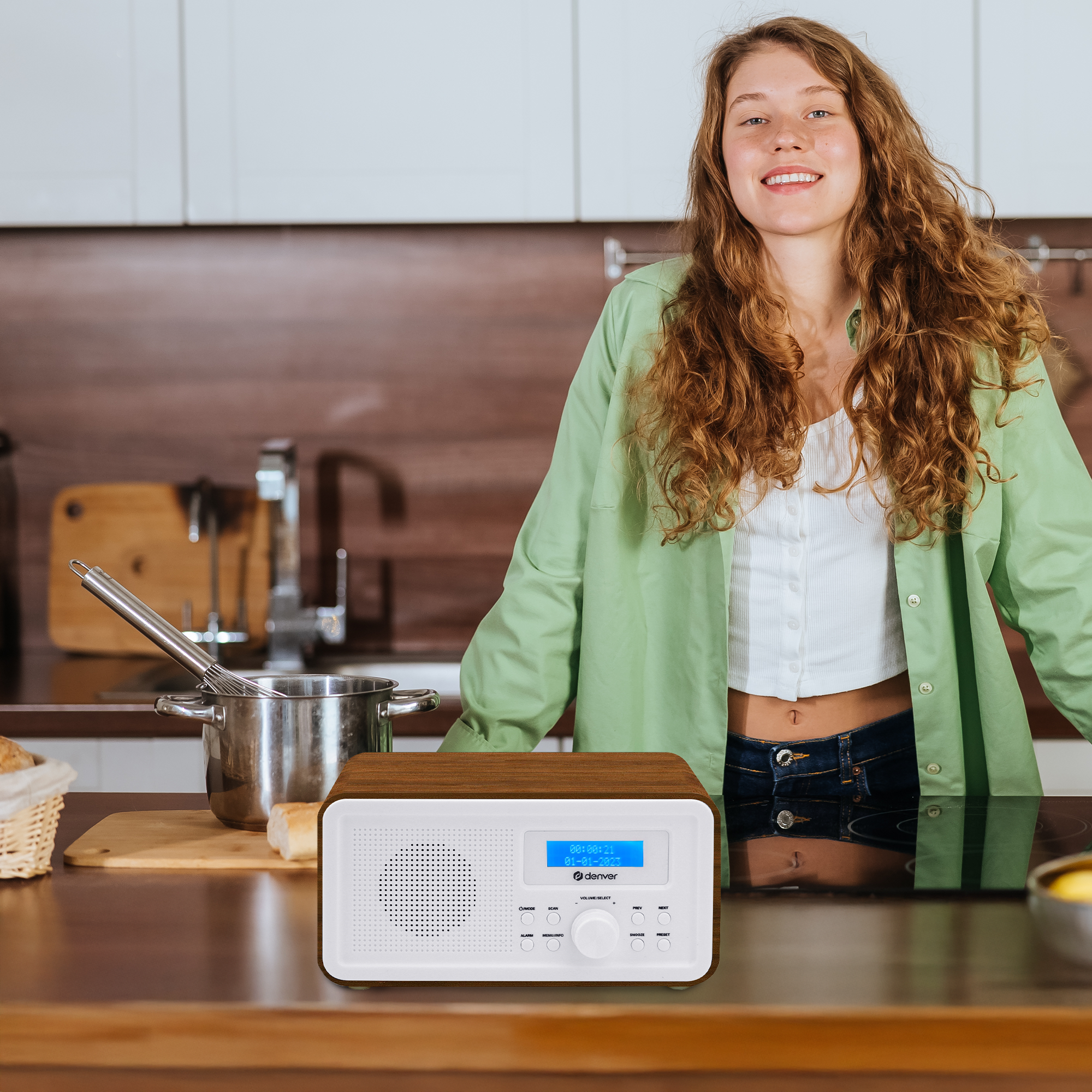 Frau in der Küche mit Radio. Holzradio auf der Theke, blaues Display, lächelnde Frau in grünem Oberteil.