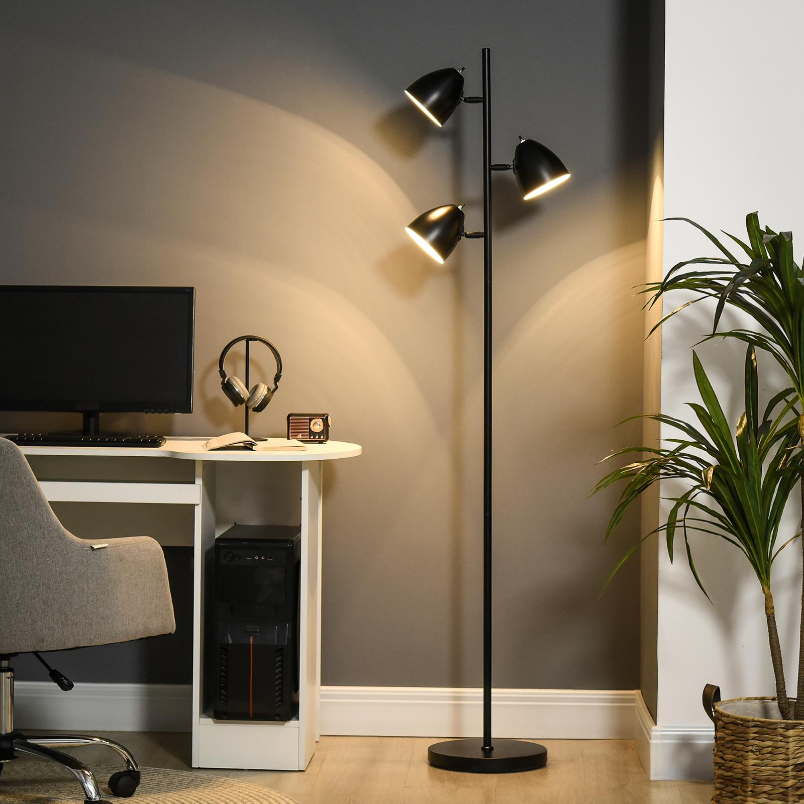 Stehlampe mit drei schwarzen Lampenschirmen und einem weißen Schreibtisch mit Zubehör in einem grau getäfelten Raum.
