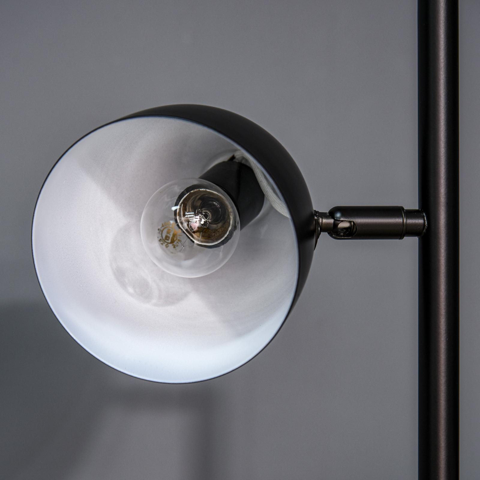 Eine schwarze Lampe mit einer sichtbaren Glühbirne im Lampenschirm, auf grauem Hintergrund.