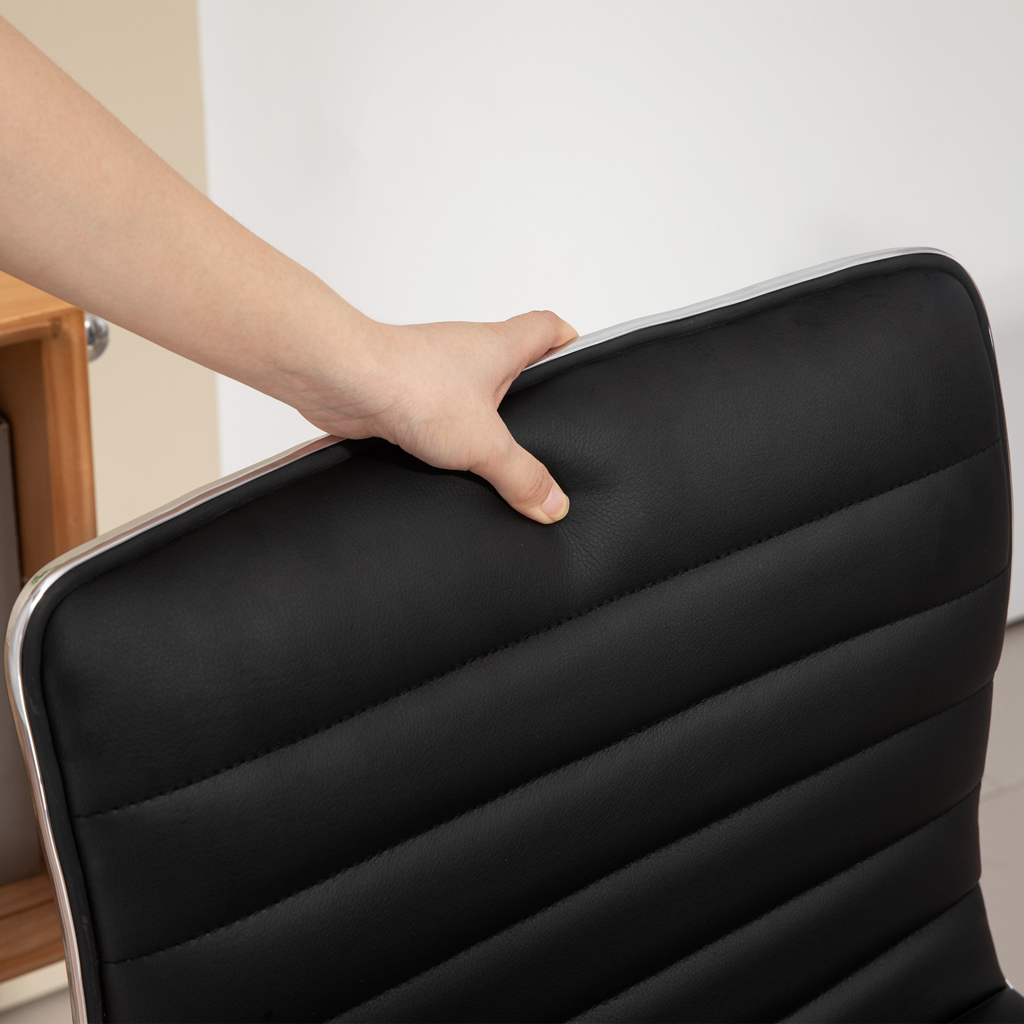 Hand hält schwarzen Stuhlrücken. Stuhl hat Chromverkleidung.